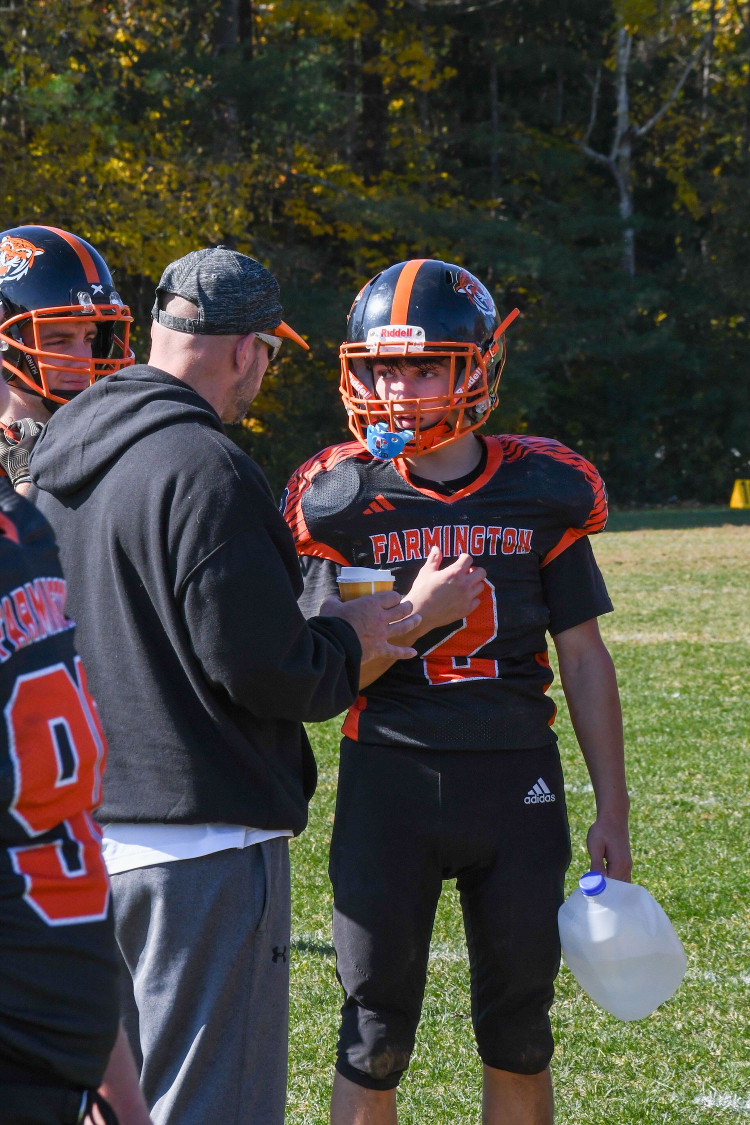 Football coach gives instructions to player in orange and black uniform during game.