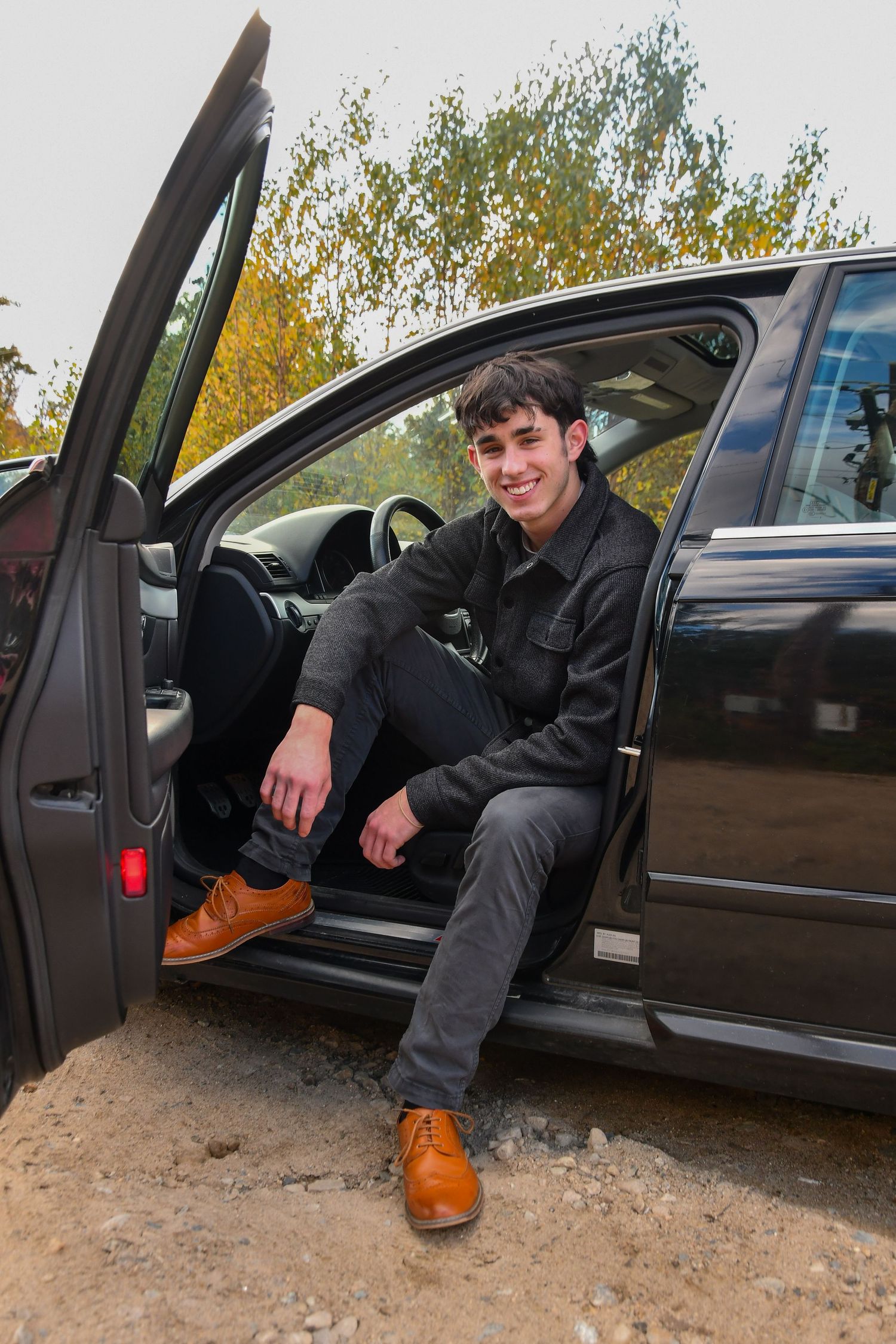 Person sitting in driver's seat of black car wearing brown boots and dark jacket.