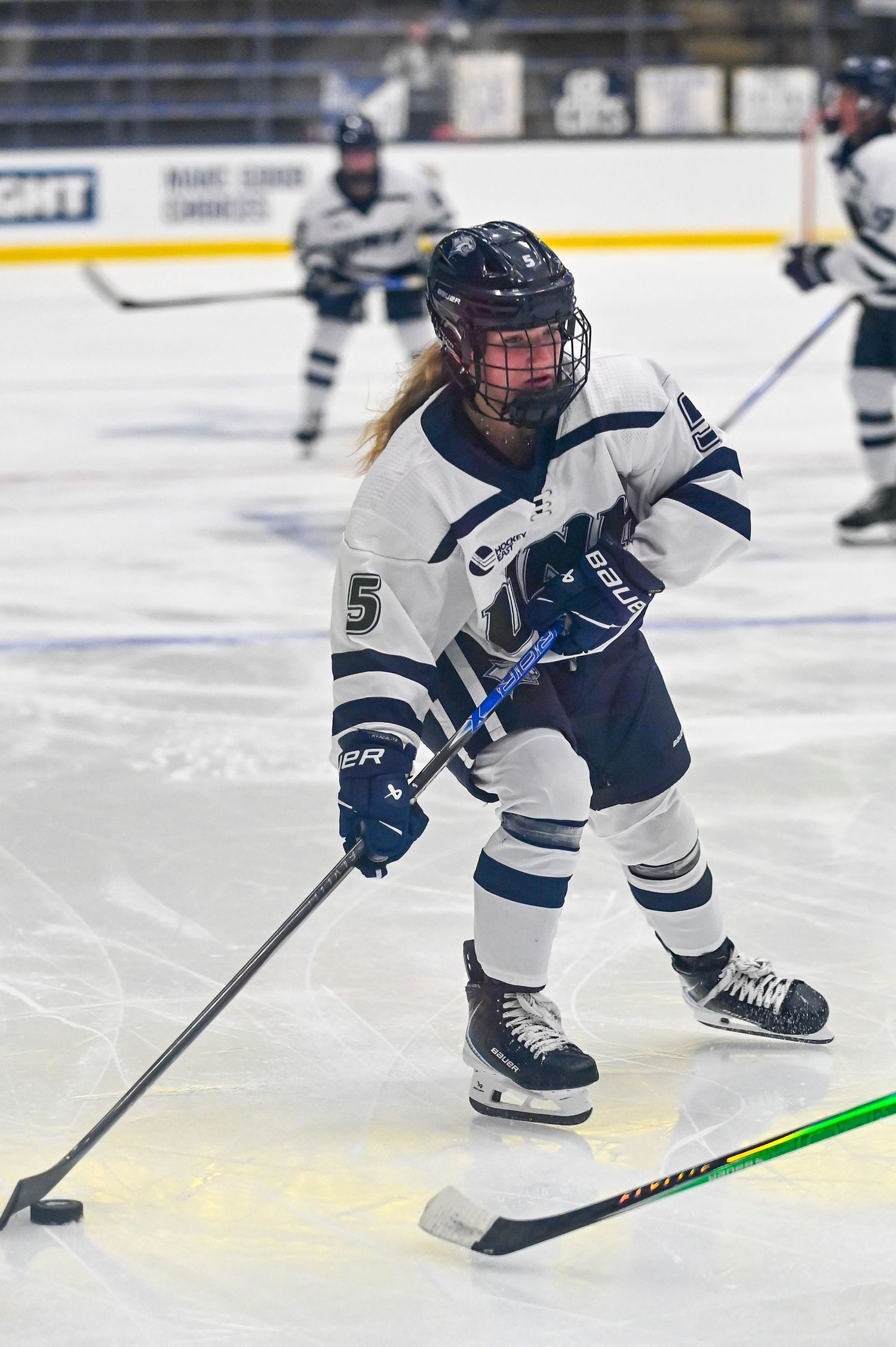 Youth hockey player in white and navy uniform skates low on ice during competitive game.