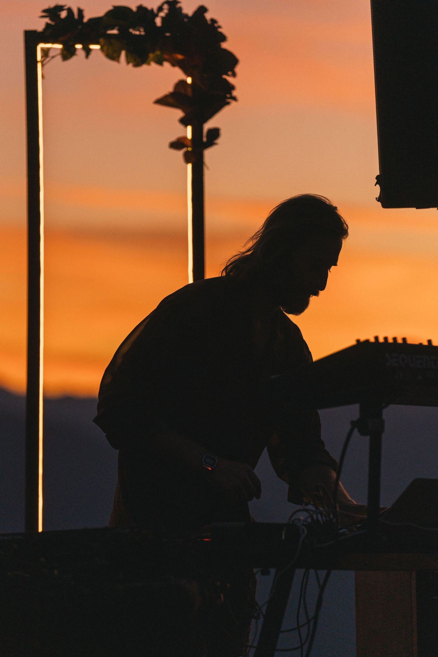 Silhouette of a musician performing on stage against a vibrant orange sunset sky.