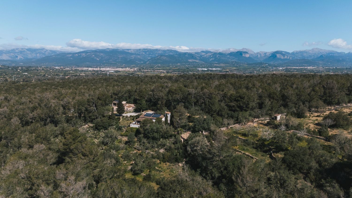 Aerial view of rural property nestled in rugged hills with mountains in the background on a sunny day.