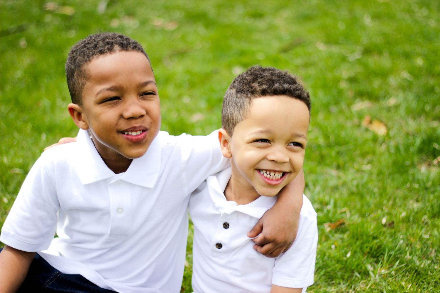 Cheerful outdoor family photos of children in white shirts on green grass.