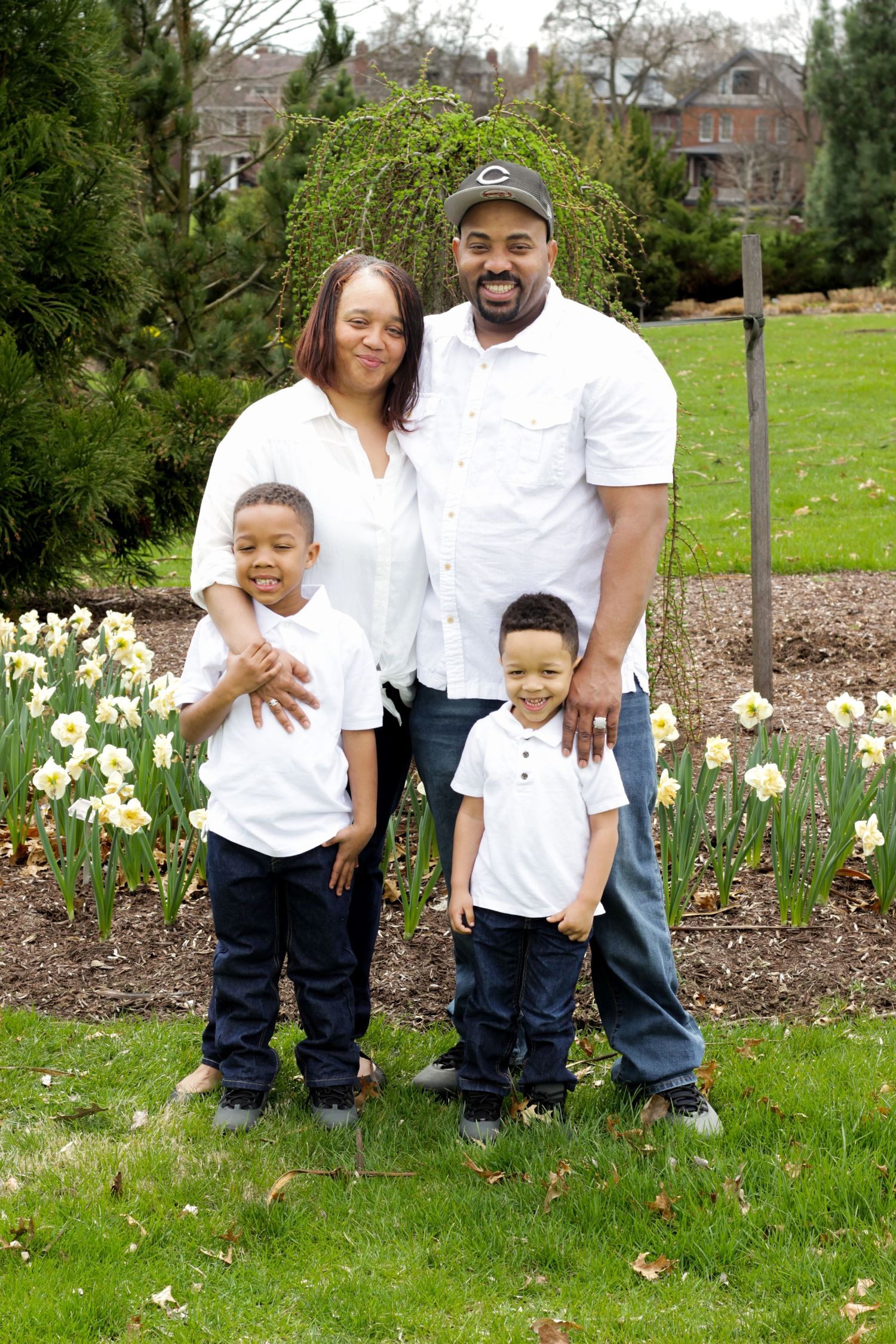 Family portrait series in coordinating white outfits by spring garden with daffodils.
