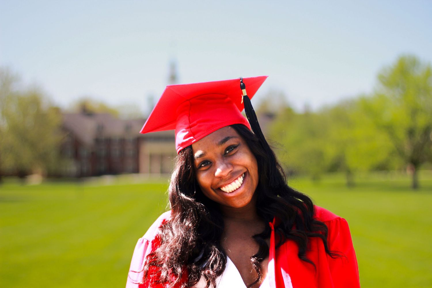 Graduation portraits with red cap and gown against a sunny outdoor backdrop.