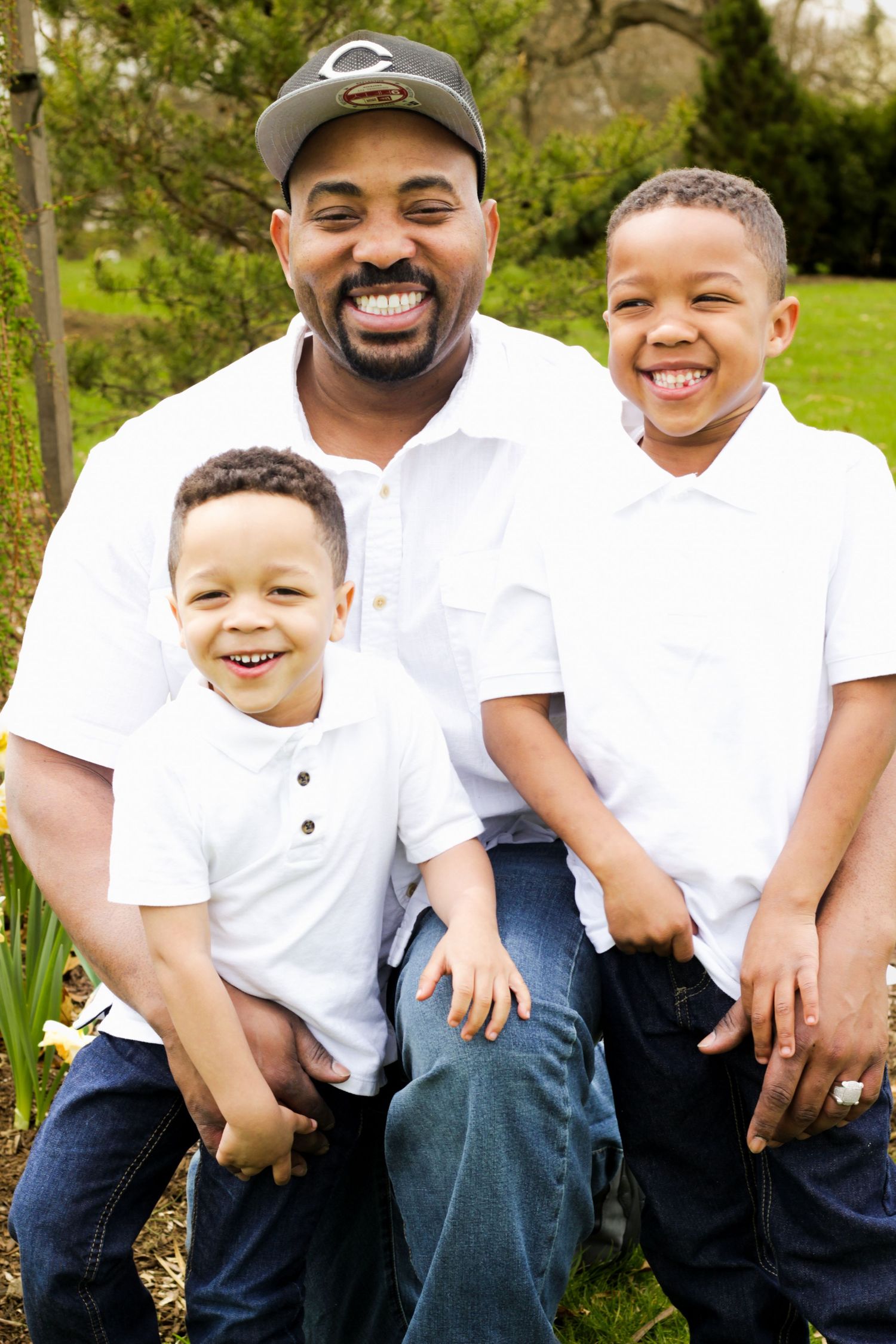 Family wearing matching white shirts and jeans sitting together outdoors in a park setting.