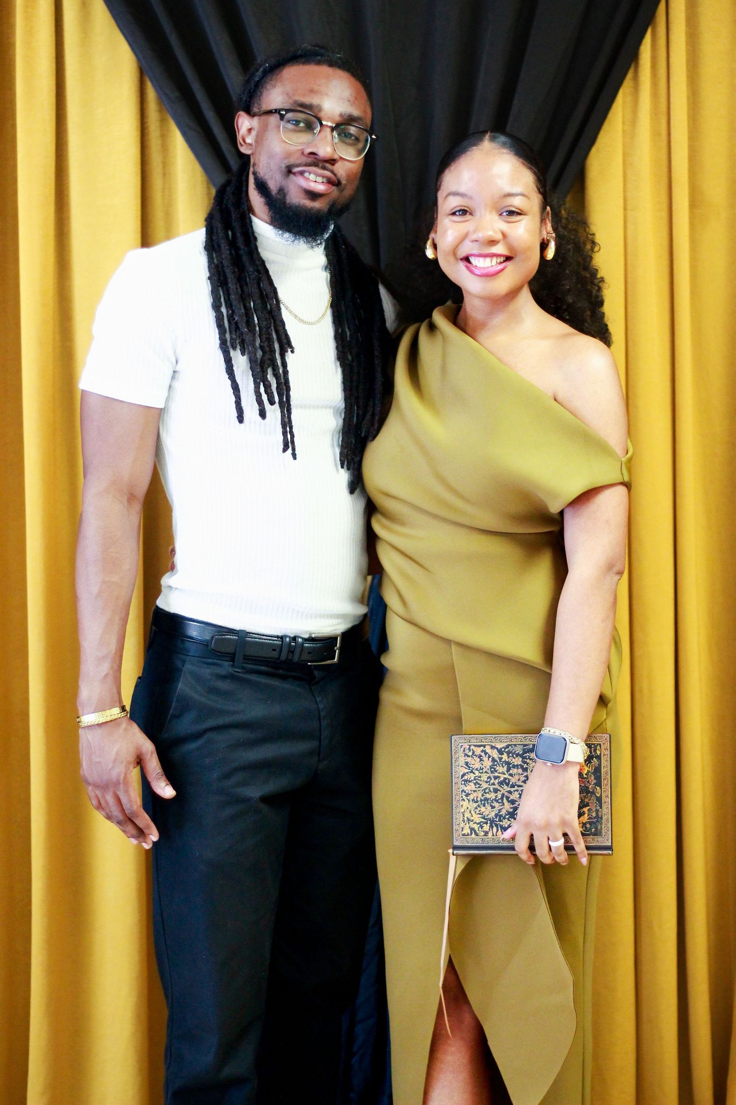 Couple posing together against yellow curtains in formal attire.
