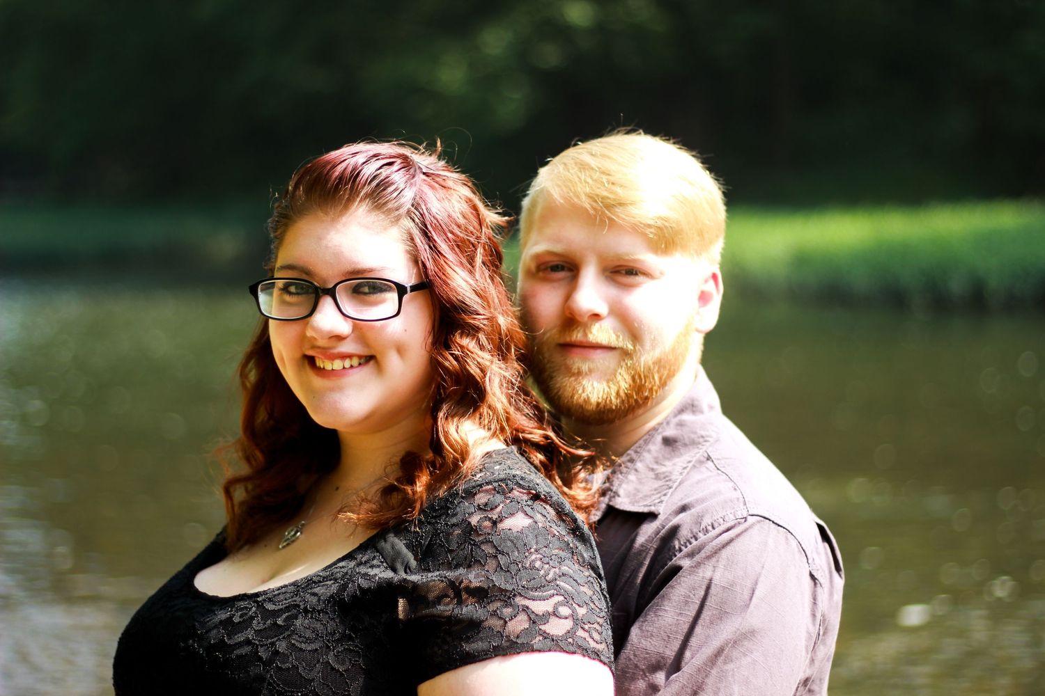 Couple poses together by lake during autumn outdoor photo session.