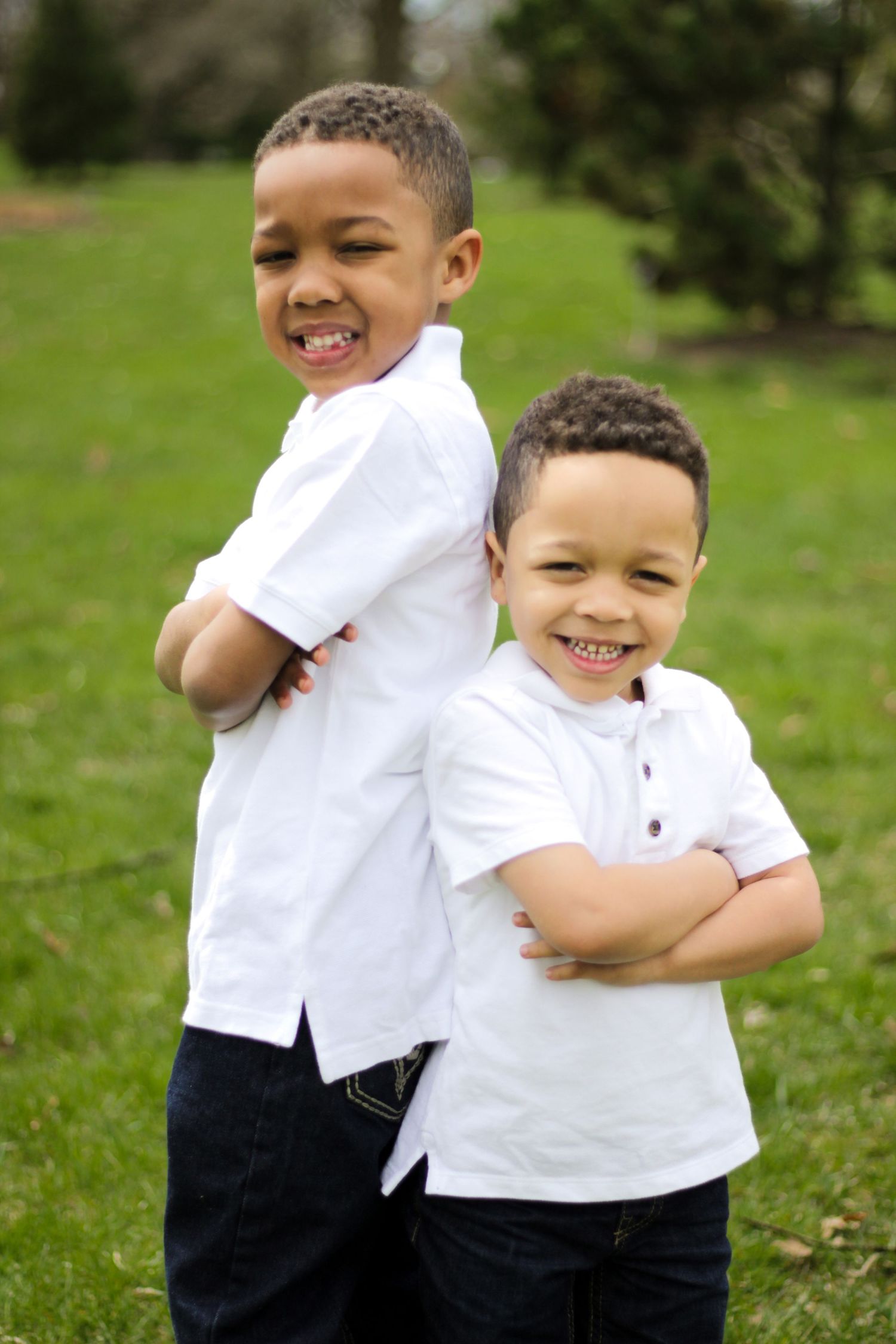 Two young children in white shirts play and laugh together on green grass.