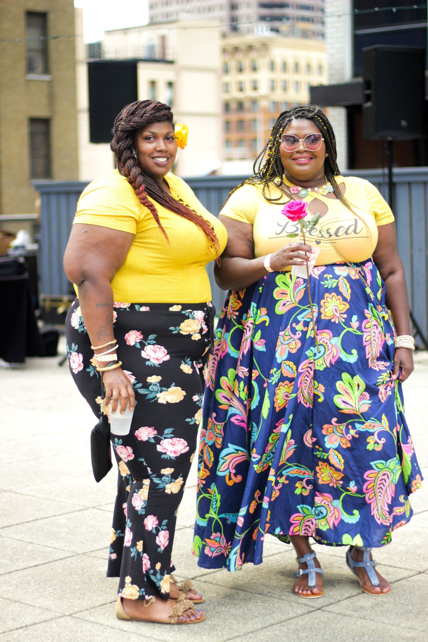Two women in coordinated yellow tops and floral skirts pose together outdoors.