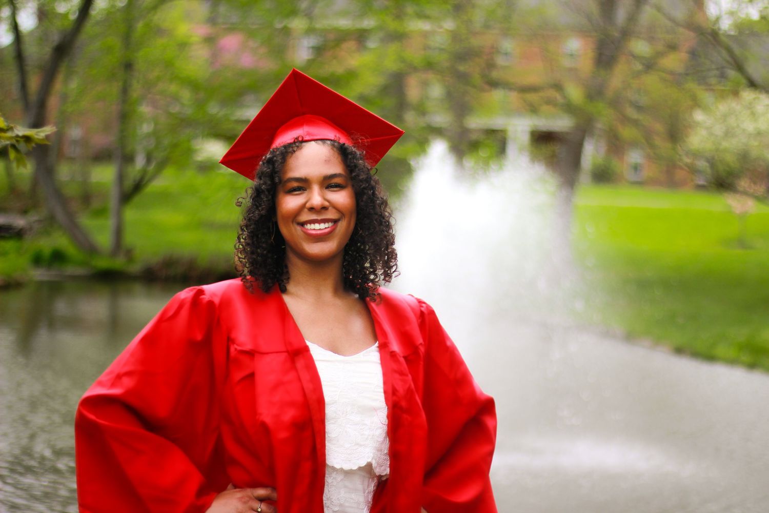 Graduate in bright red cap and gown poses outdoors for celebration photos.