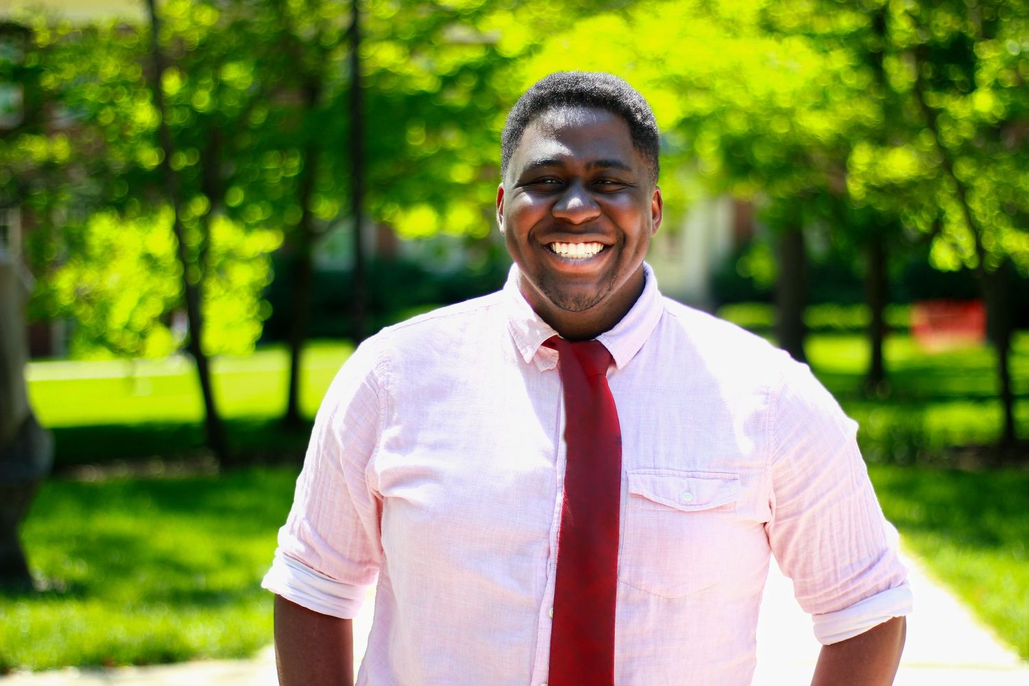 Professional outdoor portraits of someone in a crisp white shirt and red tie against a vibrant green natural background.