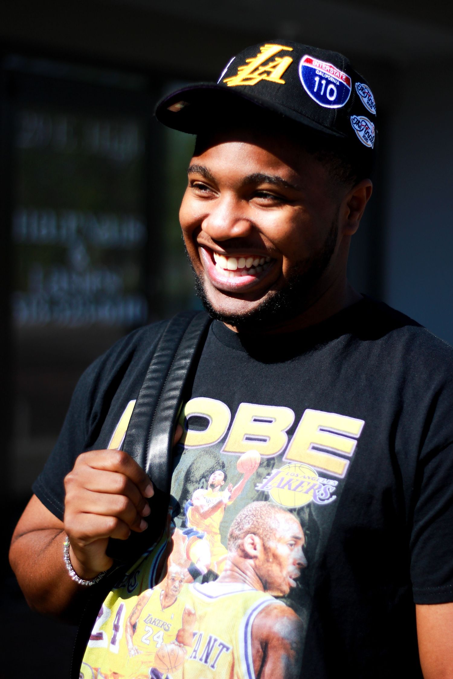 Fan in Lakers merchandise smiles and poses for photos outdoors.