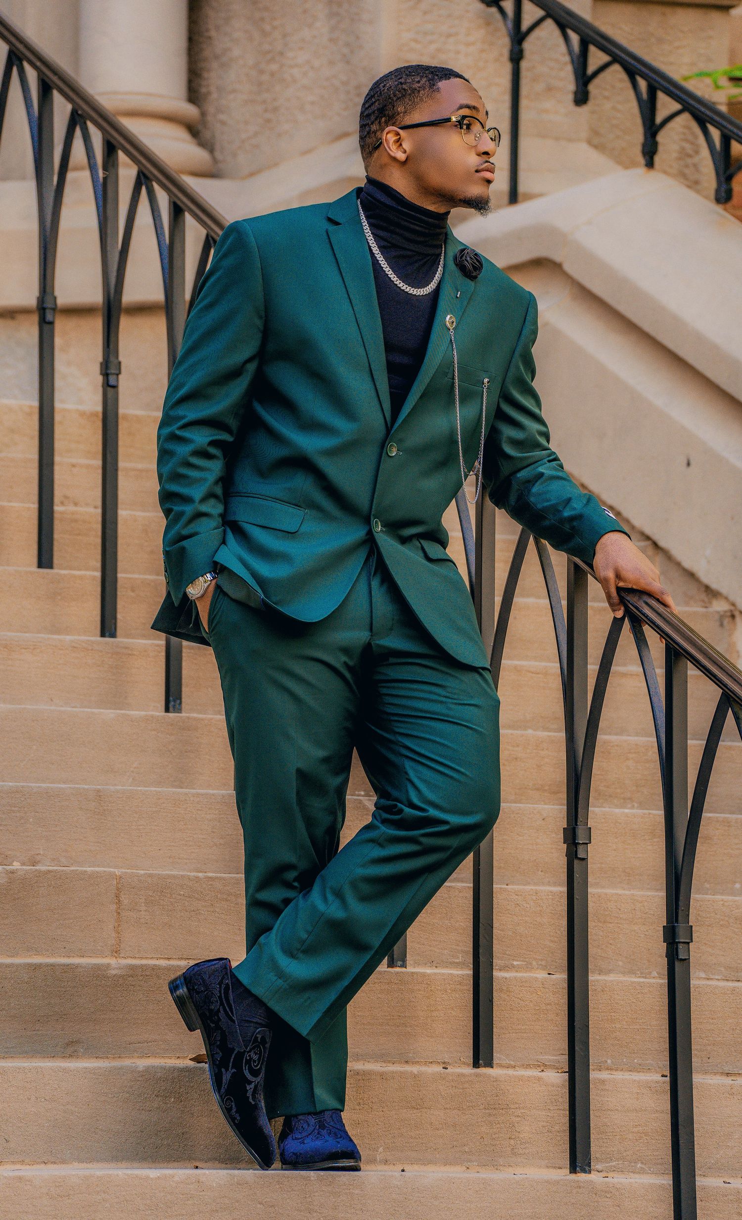 Fashionable emerald green suit styled with black turtleneck and dress shoes on stone steps with iron railing.