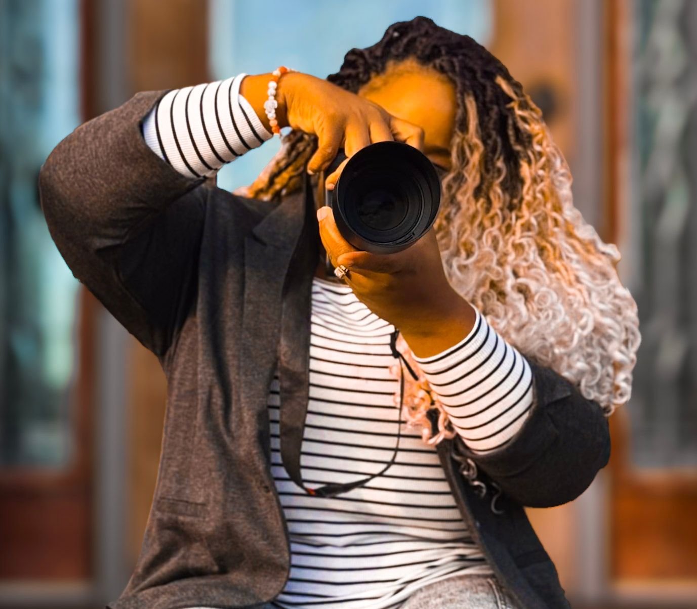 A photographer in a striped shirt and grey sweater holds up a professional camera with blurred background. Clarksville