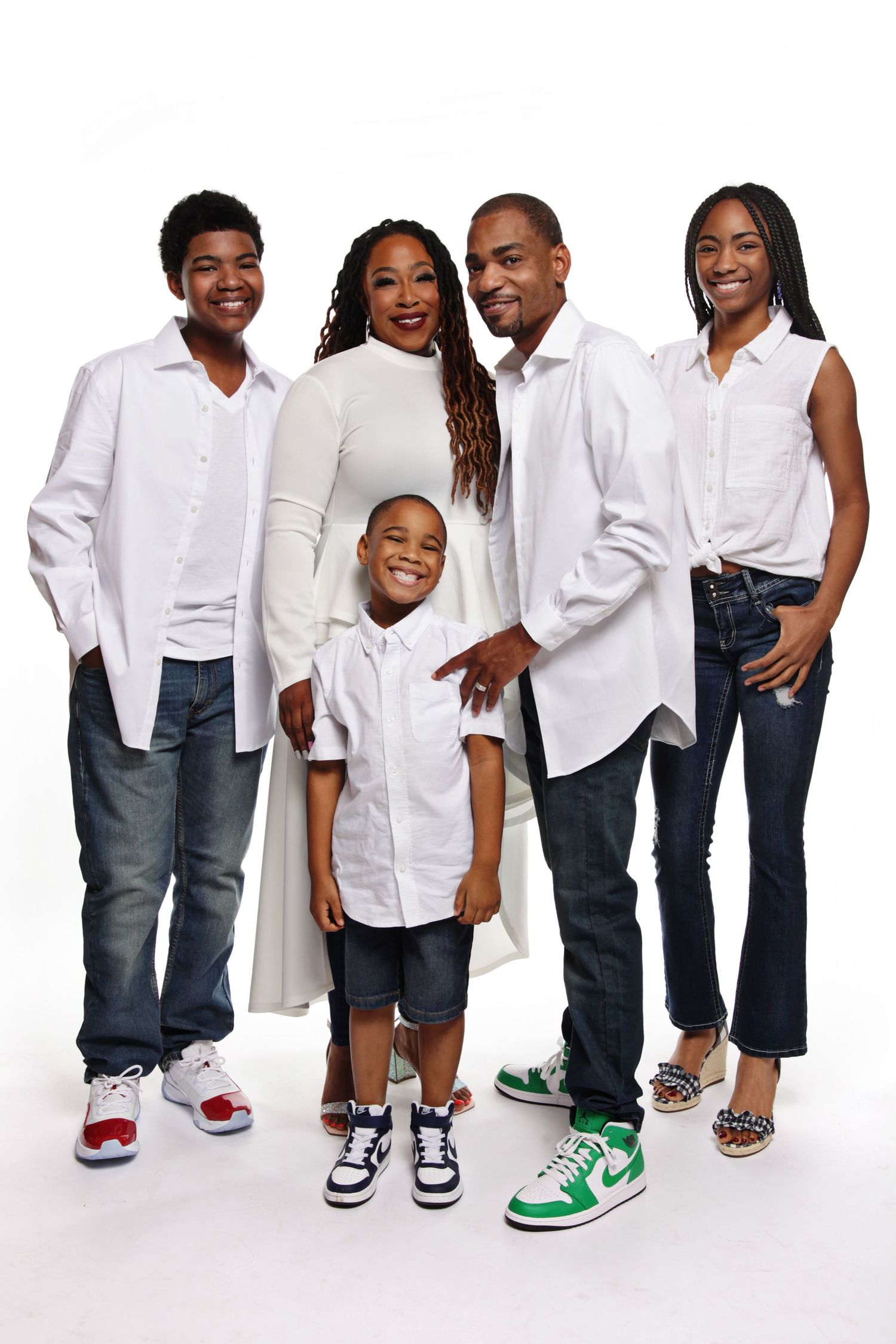 A family of five poses together in coordinated white shirts and jeans against a white background.