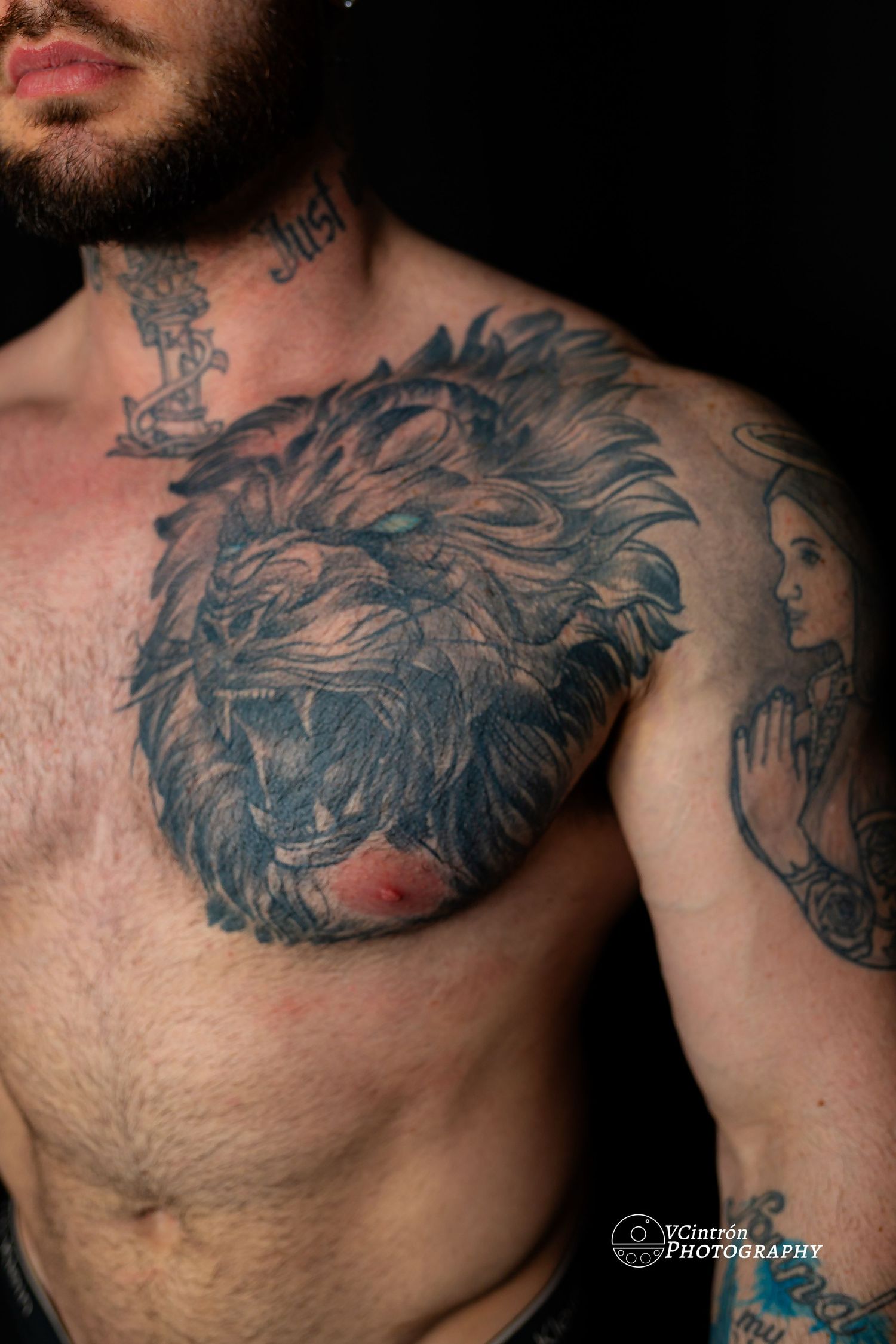 Close-up photo of a detailed lion head tattoo with fierce expression on a man's chest, done in dark gray ink.