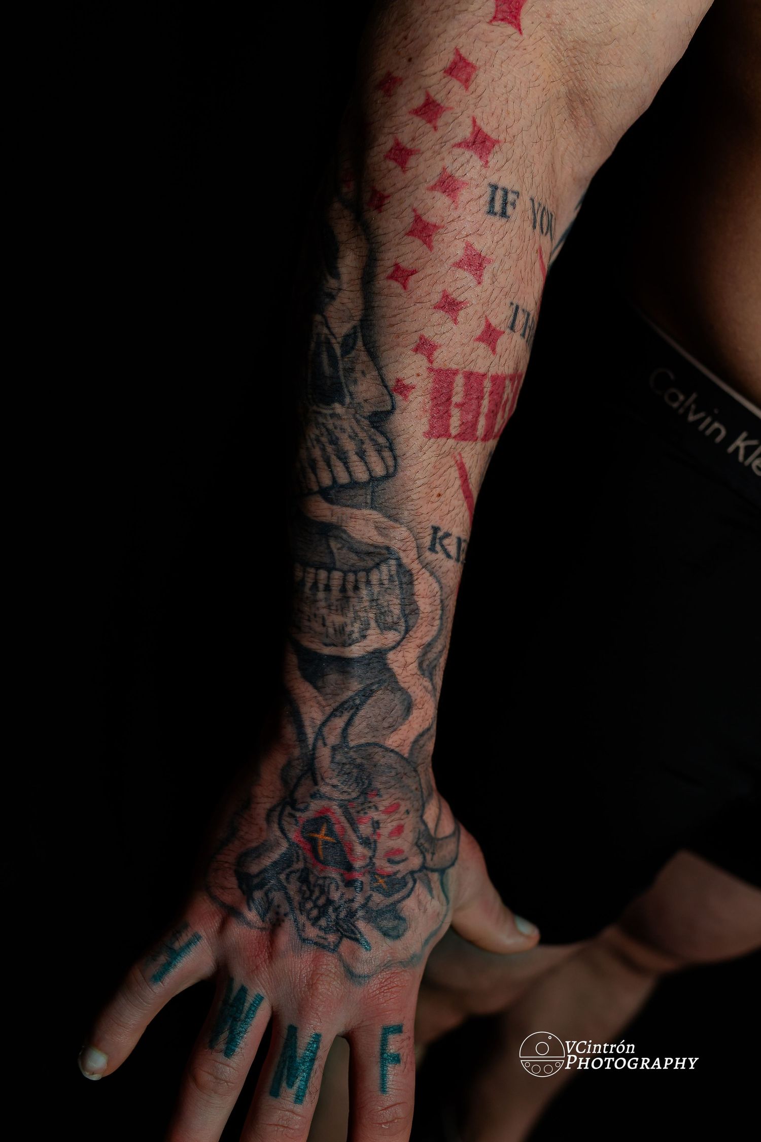Close-up photo of an artistic arm tattoo featuring red stars and black designs extending from hand to forearm.