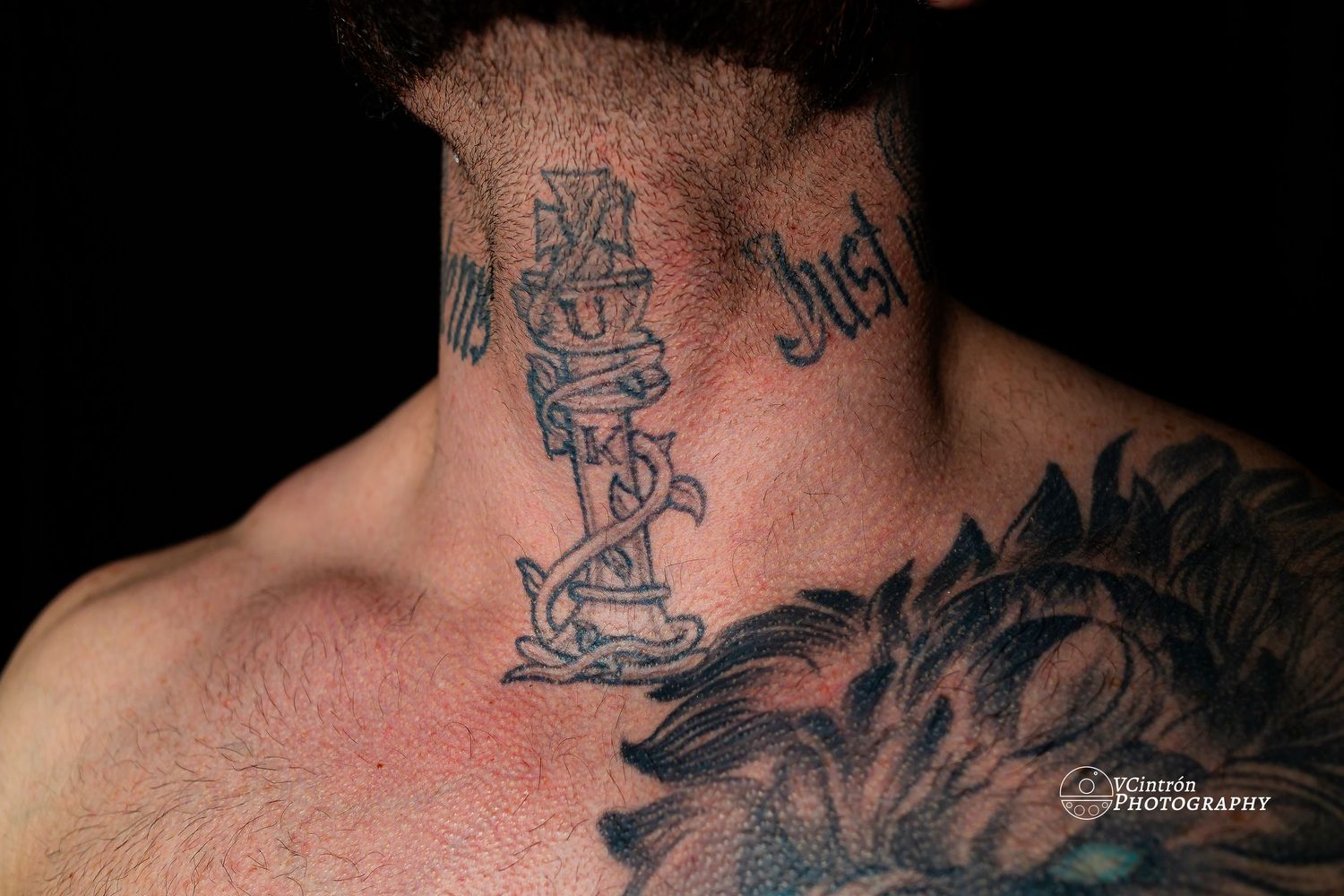 Close up of black neck tattoos showing partial designs on skin with red undertones in dark lighting.