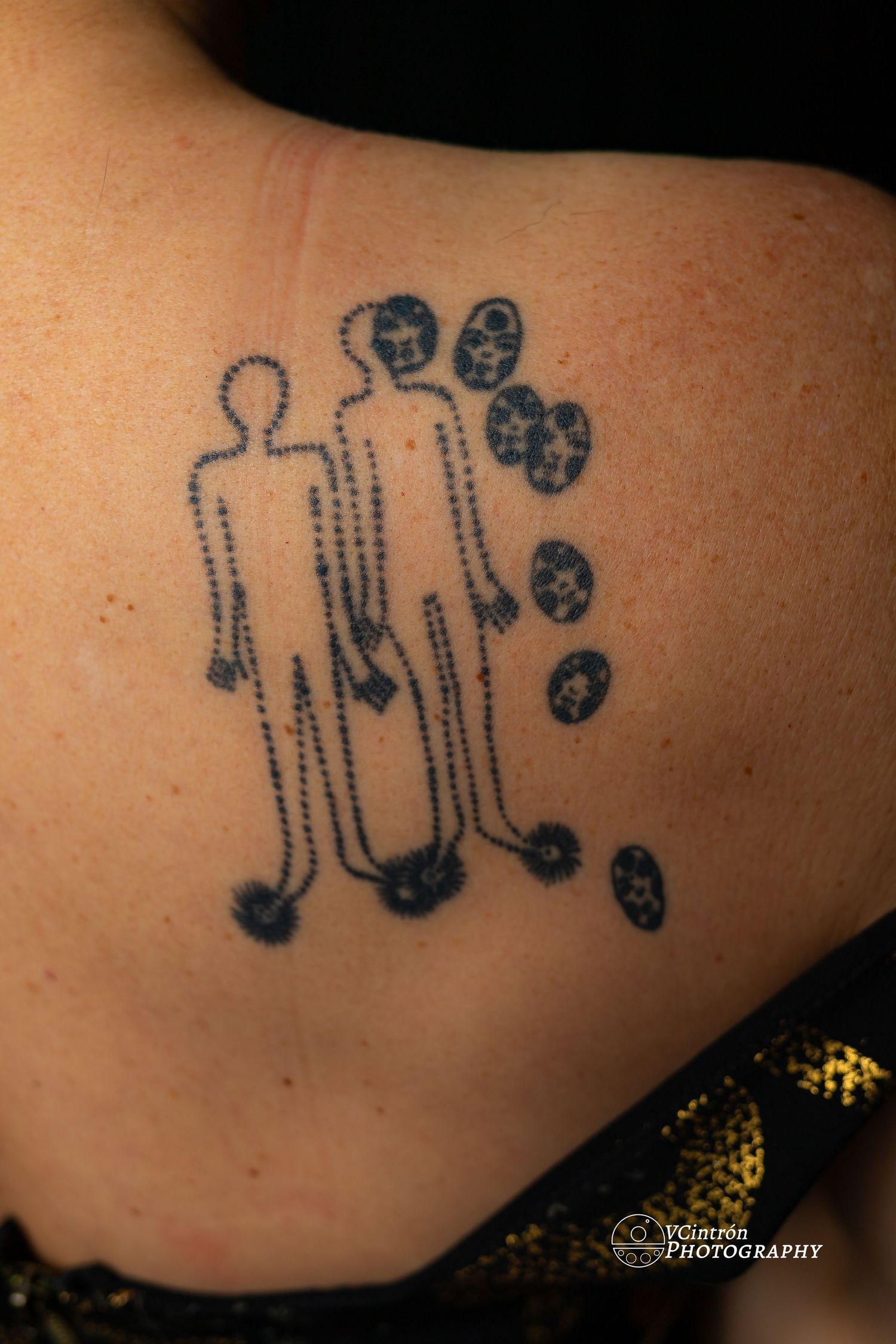Simple dotted line tattoo showing two minimalist stick figure silhouettes with trailing dots on skin.