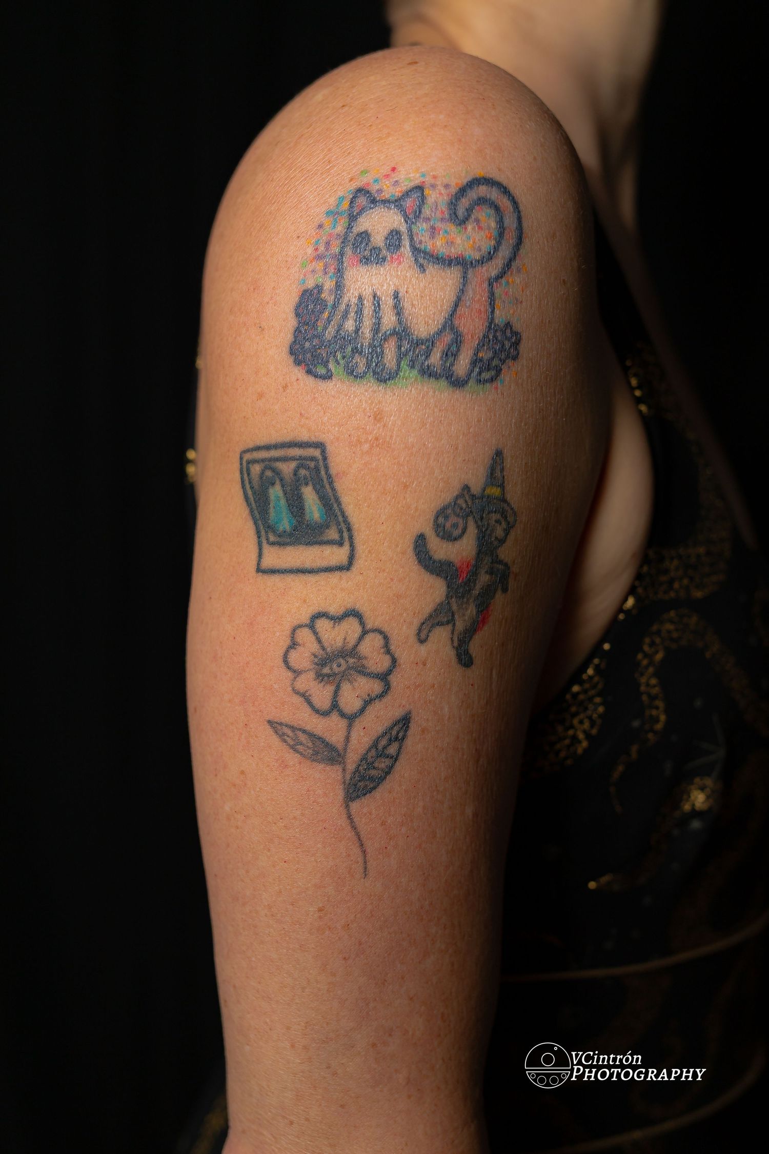 Multiple small tattoos decorate an arm including a cat, flower, puppy, and framed artwork in blue and black ink.