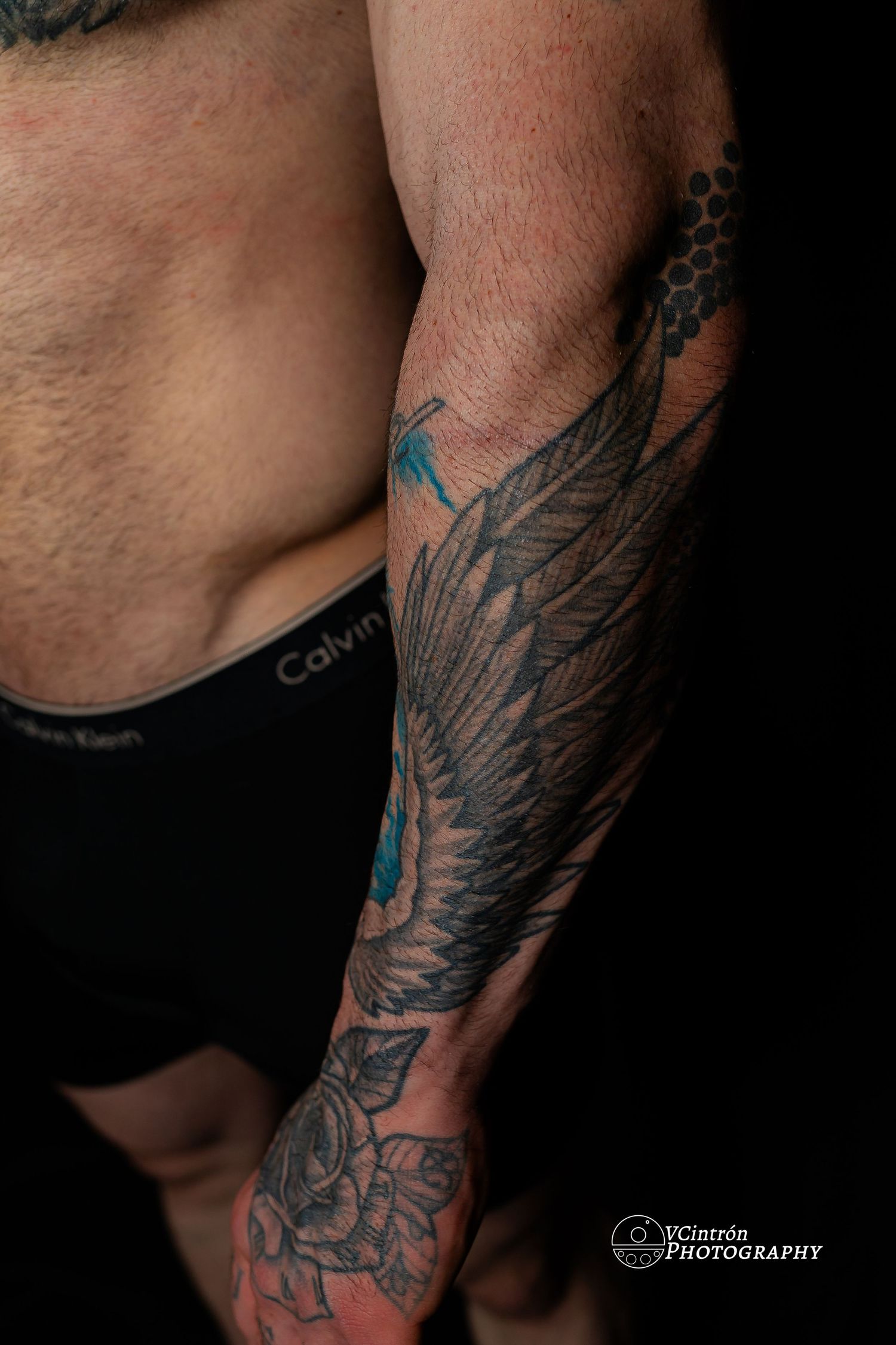 Close-up of a detailed wing tattoo with floral designs covering the forearm in black and gray ink with blue accents.