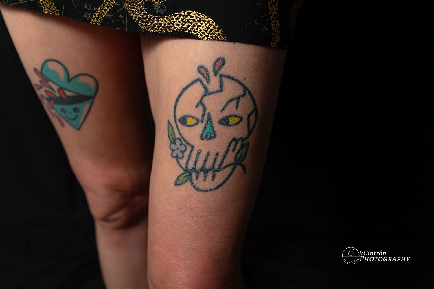 Two turquoise tattoos on legs showing a heart design and a cartoon skull with crown design.
