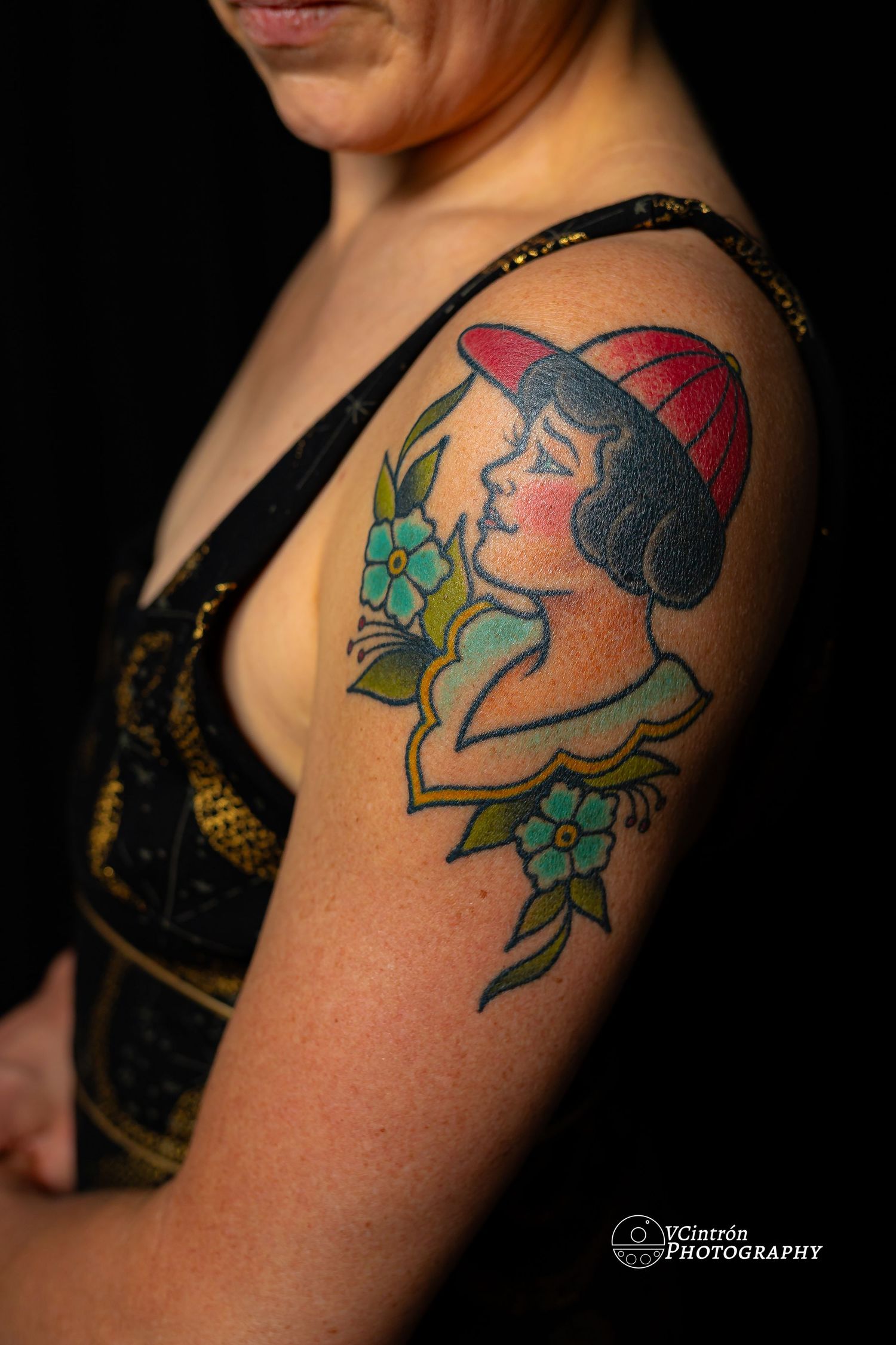 Traditional style tattoo showing a profile wearing a red cap with blue flowers and leaves on an upper arm.