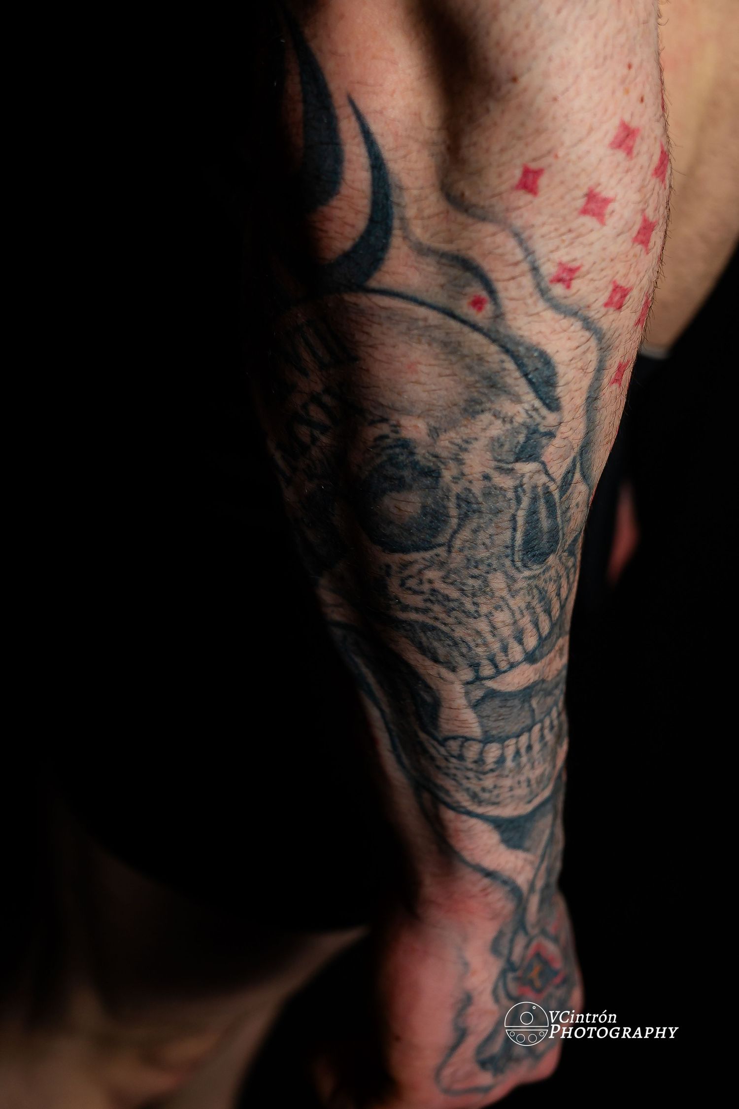 Dark tattoo artwork of a skull with sharp teeth and tribal designs on someone's forearm.