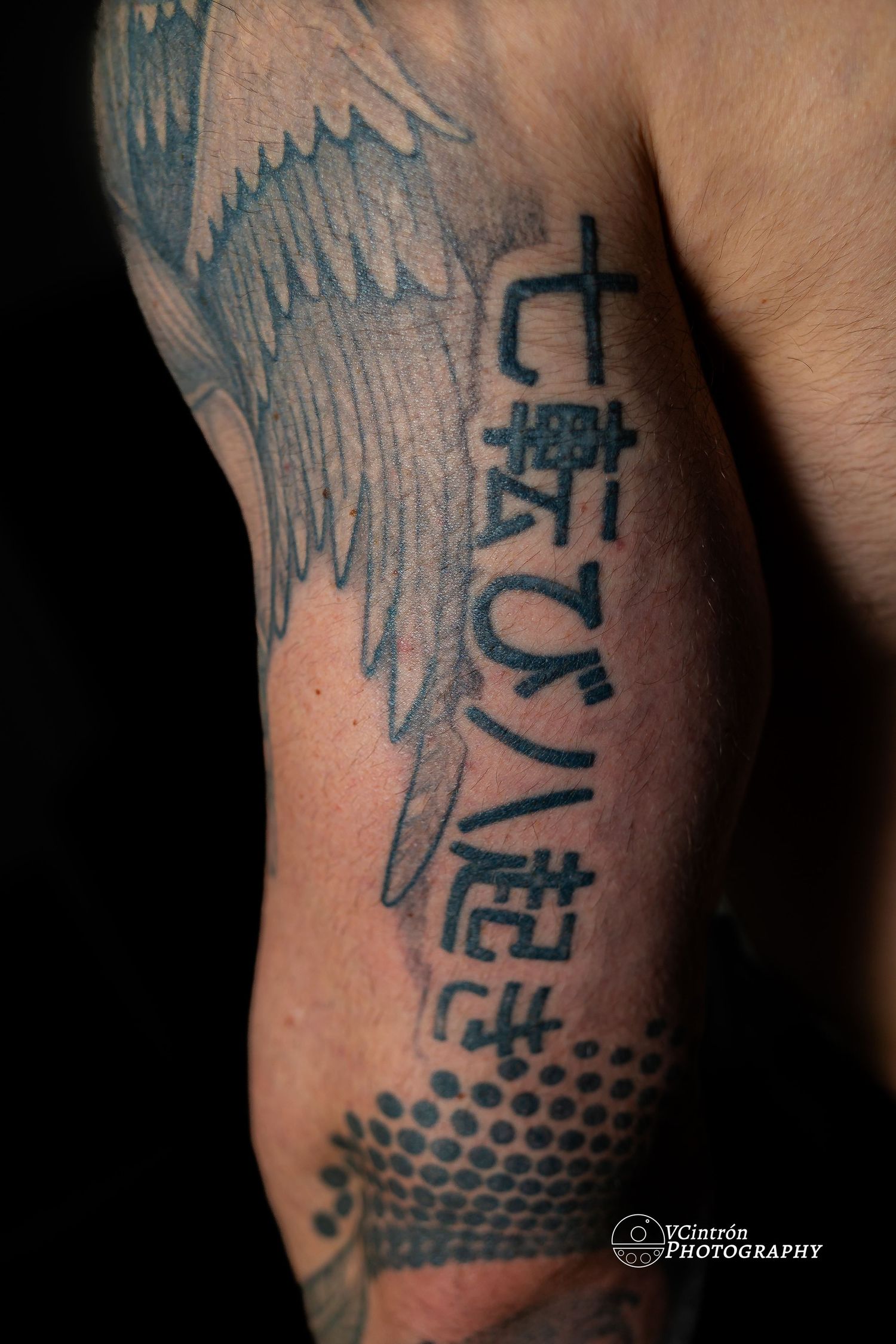 Black wing and Japanese character tattoo design with dotted pattern on person's arm.