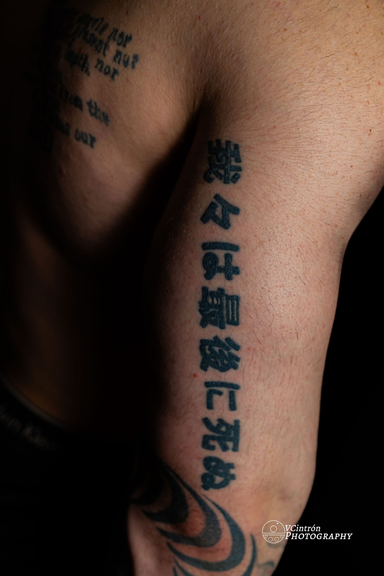 Close-up shot of Chinese characters tattooed vertically on skin with dark tribal design visible at bottom.