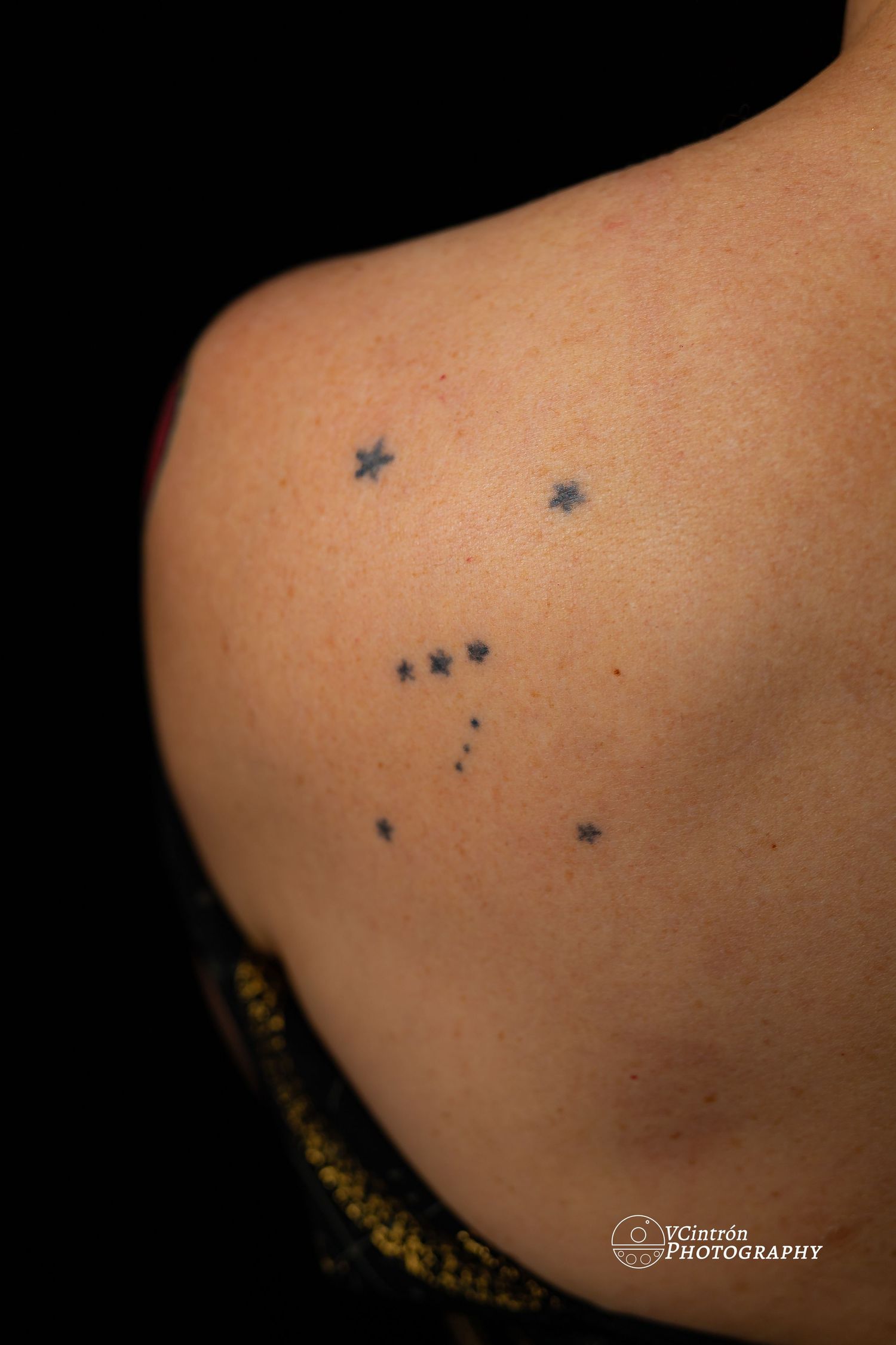 Small constellation tattoo design featuring star patterns arranged on bare skin against dark background.