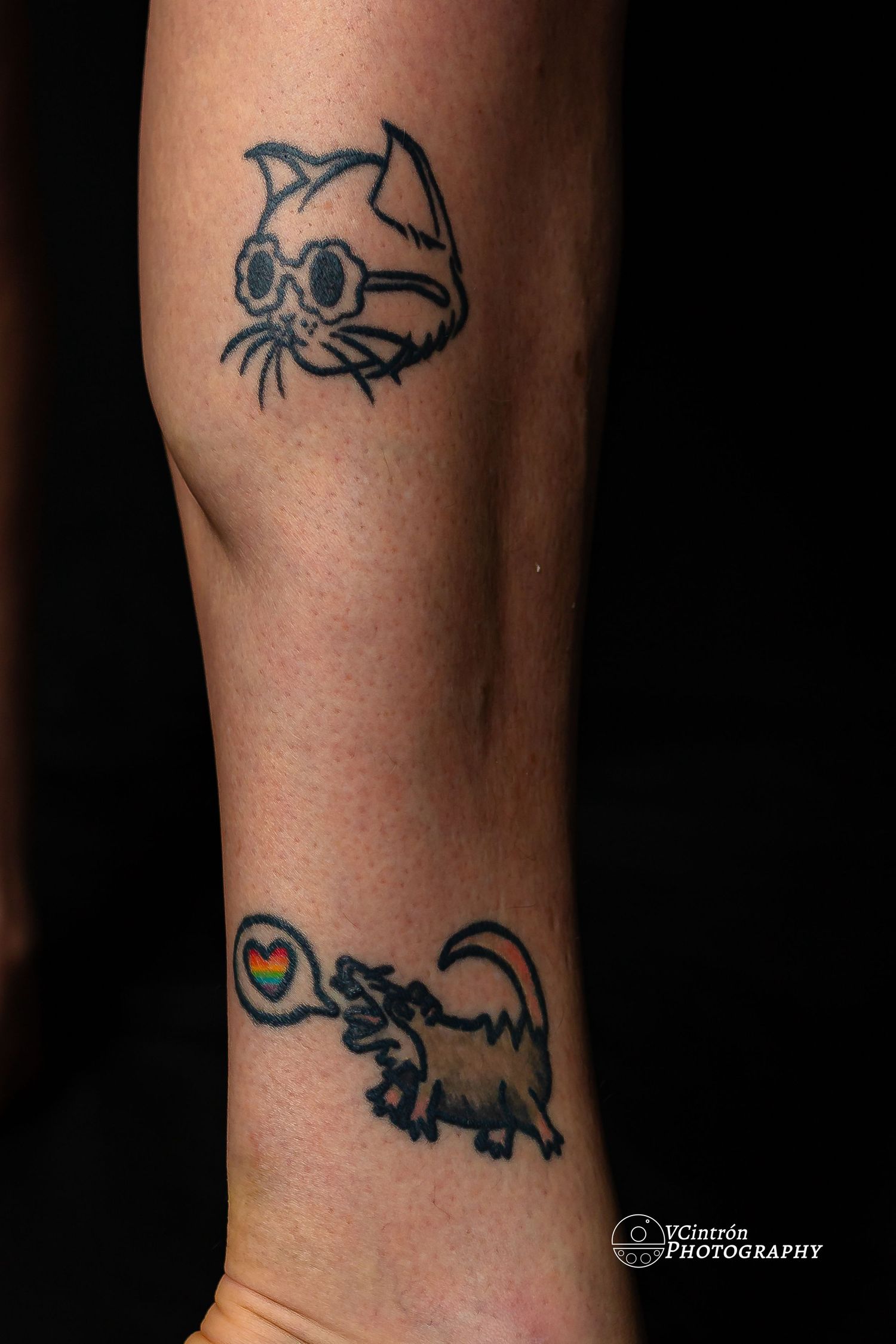 Two cat-themed tattoos on an arm showing a simple head design at top and a full cat with heart speech bubble below.
