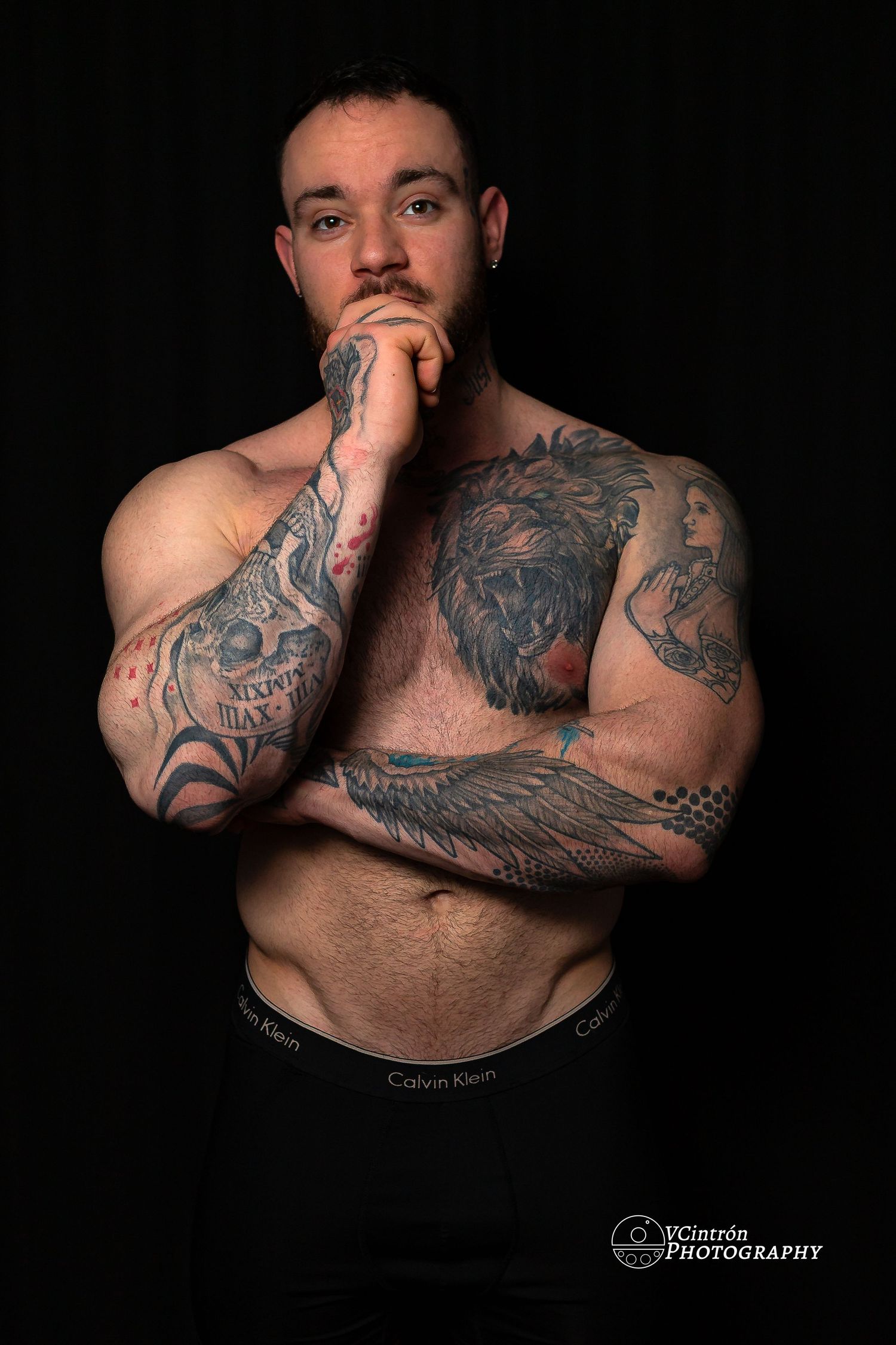 Artistic studio portrait of a shirtless muscular person with elaborate tattoos against a dark background.
