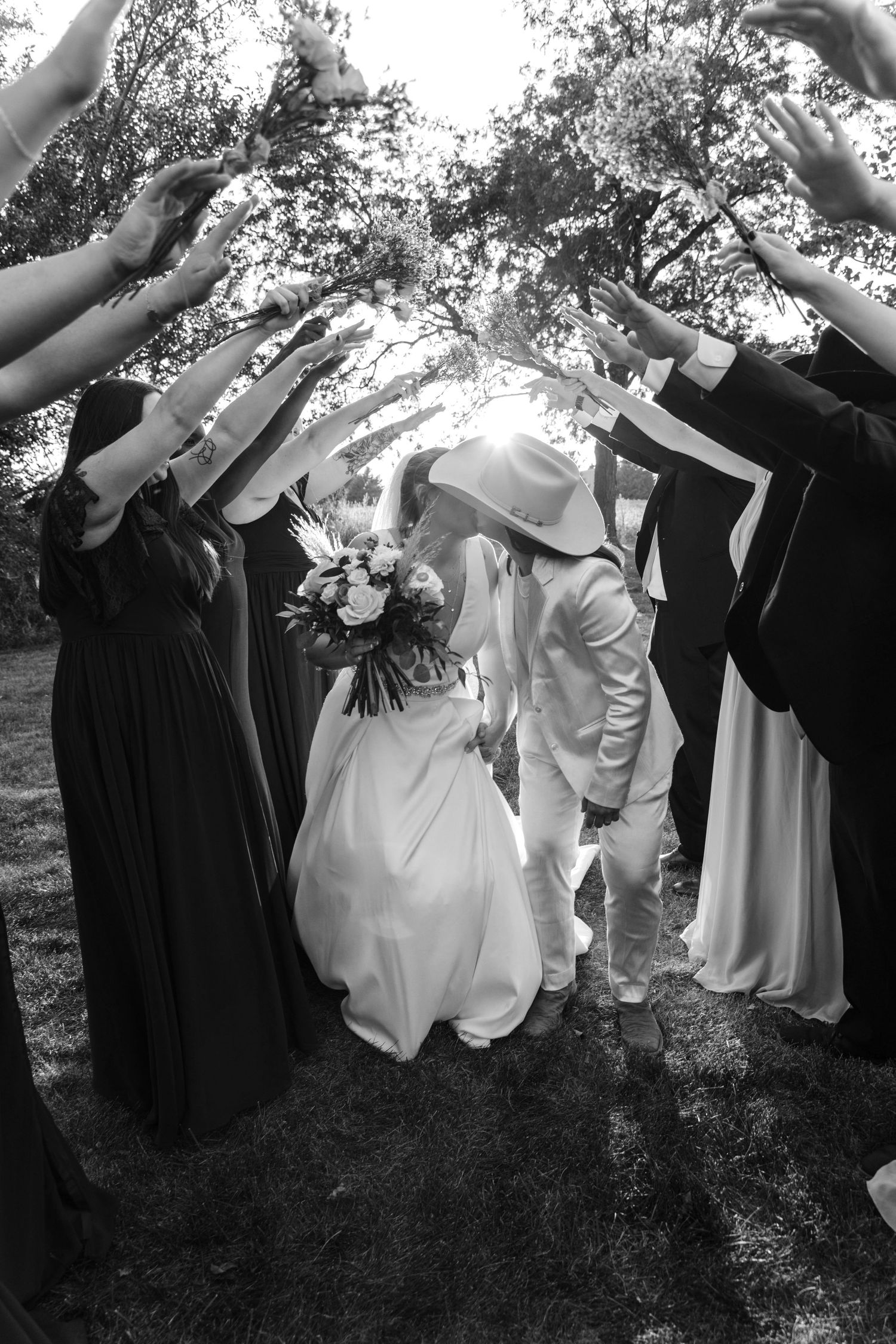 Wedding party forms a tunnel of raised arms for the newlyweds walking underneath in elegant black and white photograph.
