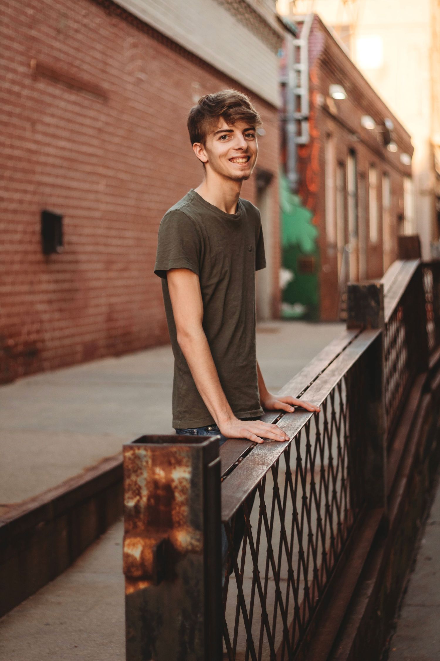 A portrait of a casual young person leaning on a metal railing in an urban setting.
