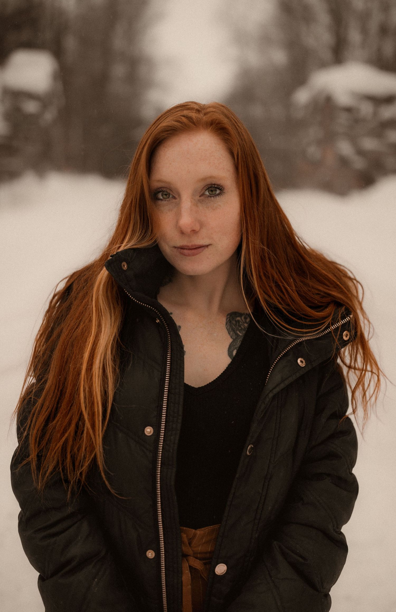 Portrait of someone with long red hair wearing a black winter coat standing in snowy outdoor setting.