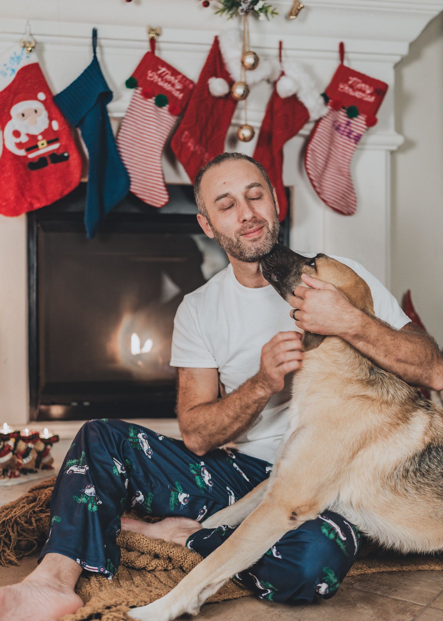 Father sharing a quiet moment with his dog beside a decorated Christmas fireplace during an at-home holiday session in Austin, Texas.