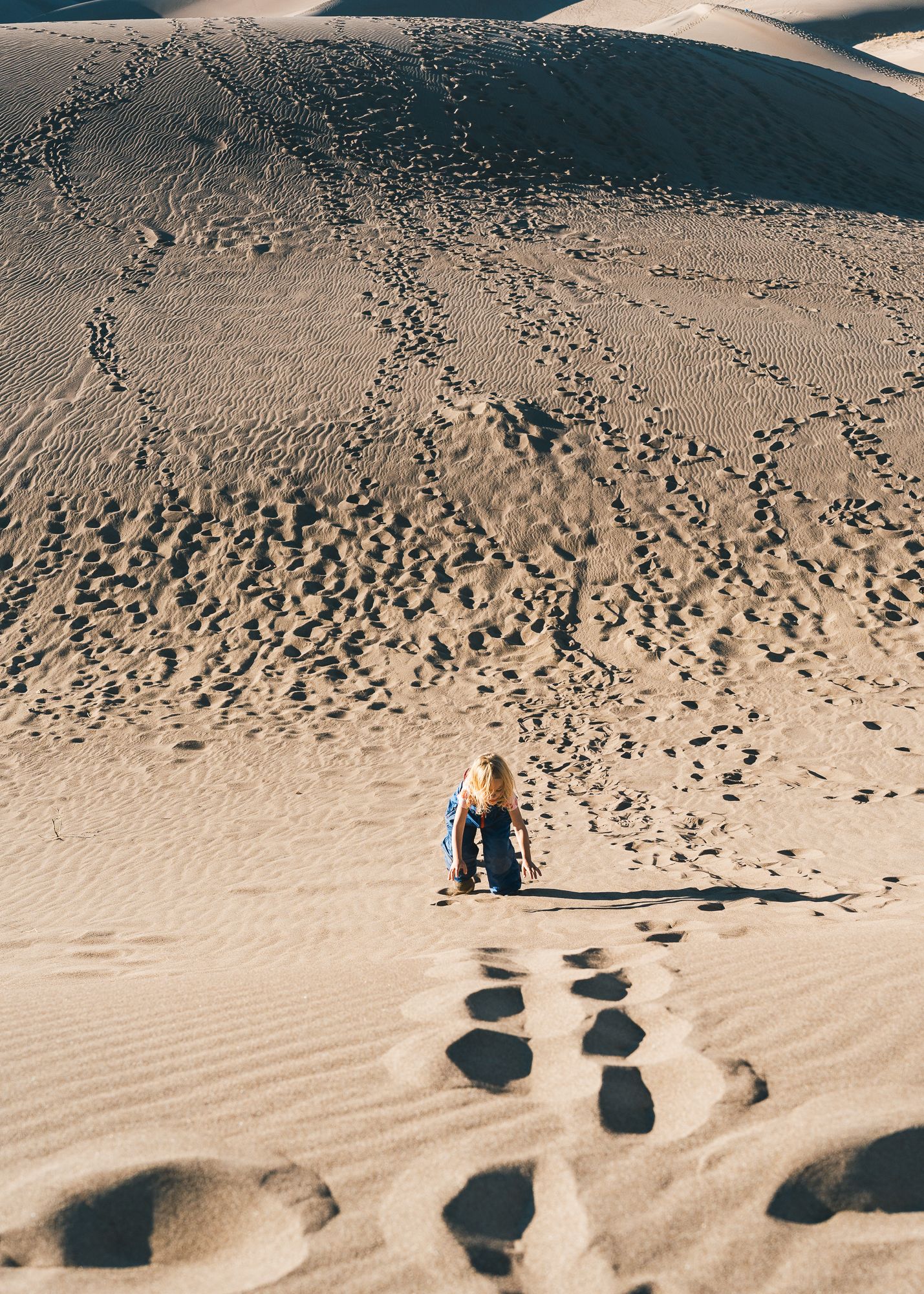 Child walking across sand dunes with footprints ahead of her