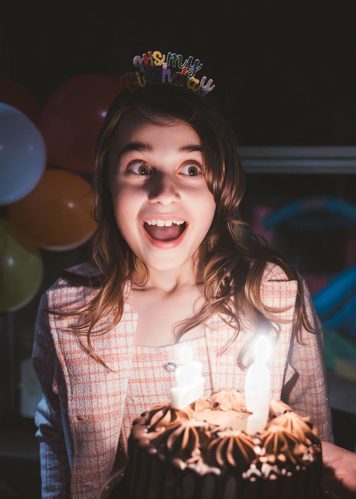 A girl smiling over a birthday cake with glowing candles during an evening celebration