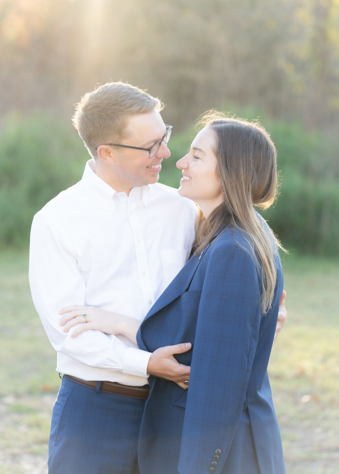 Couple smiling at each other outdoors in golden light, a blue jacket draped around her shoulders.