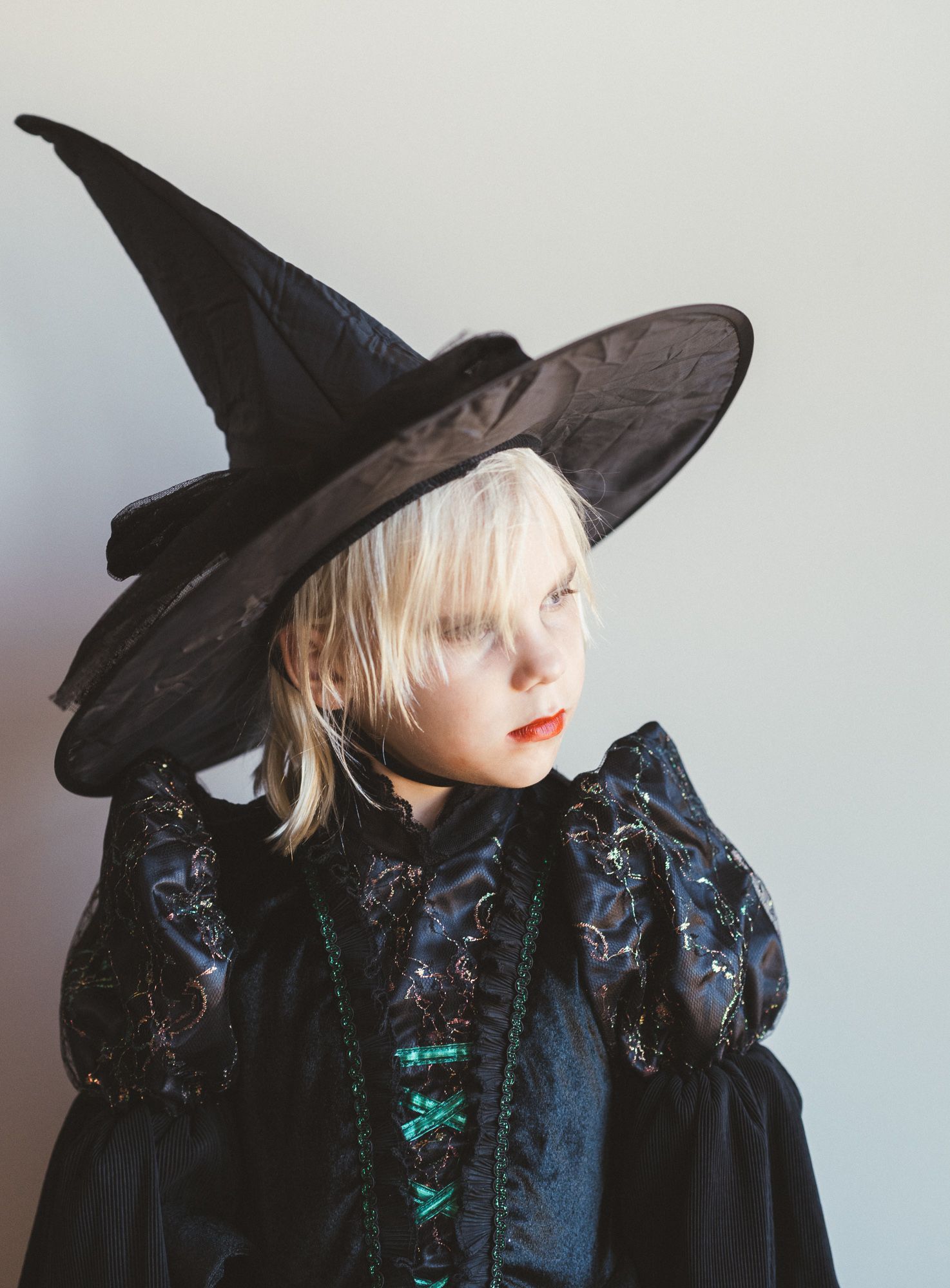 Child in a black witch hat and costume looking to the side in soft natural light.