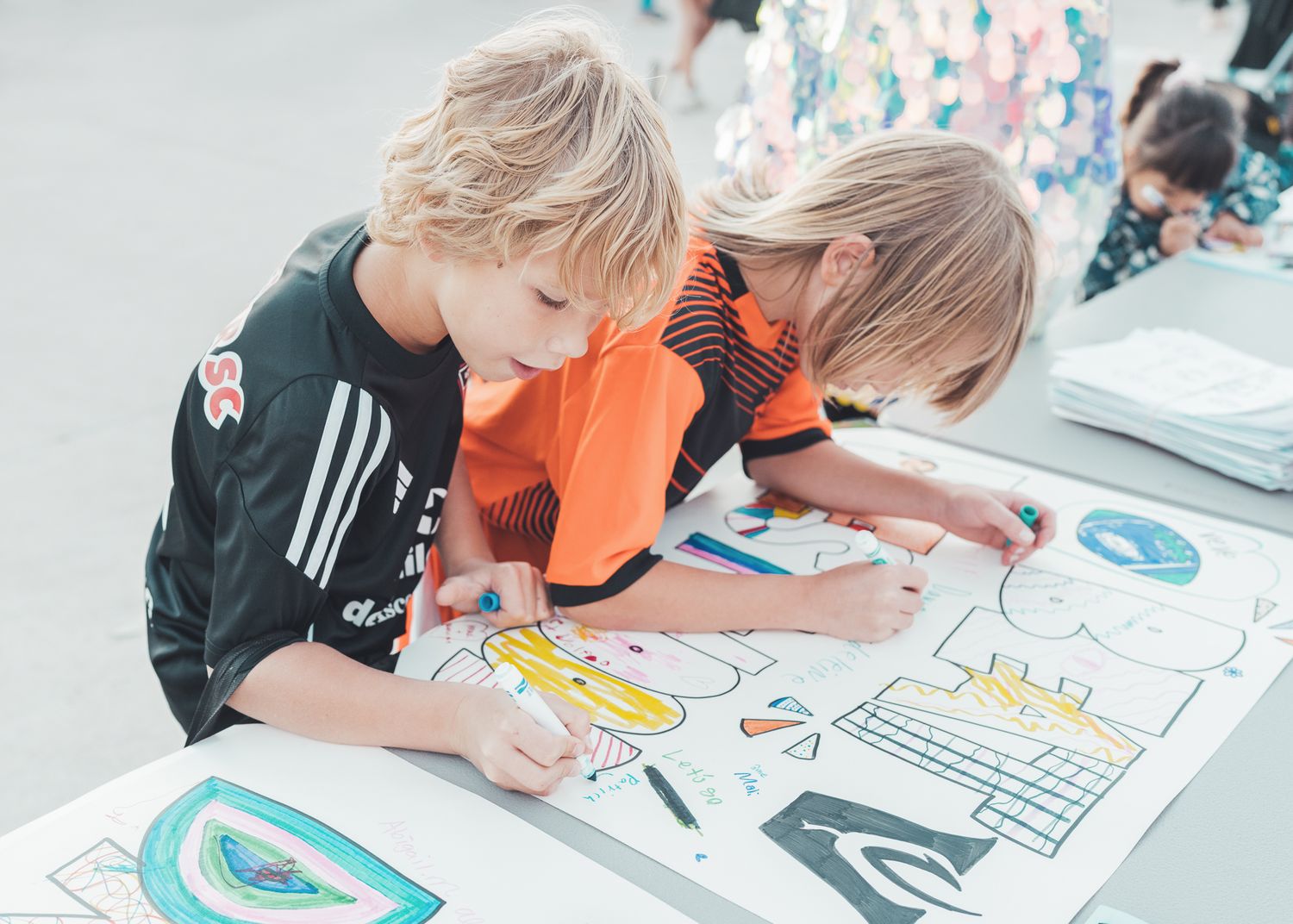 Two children drawing and coloring together at a table during a community event