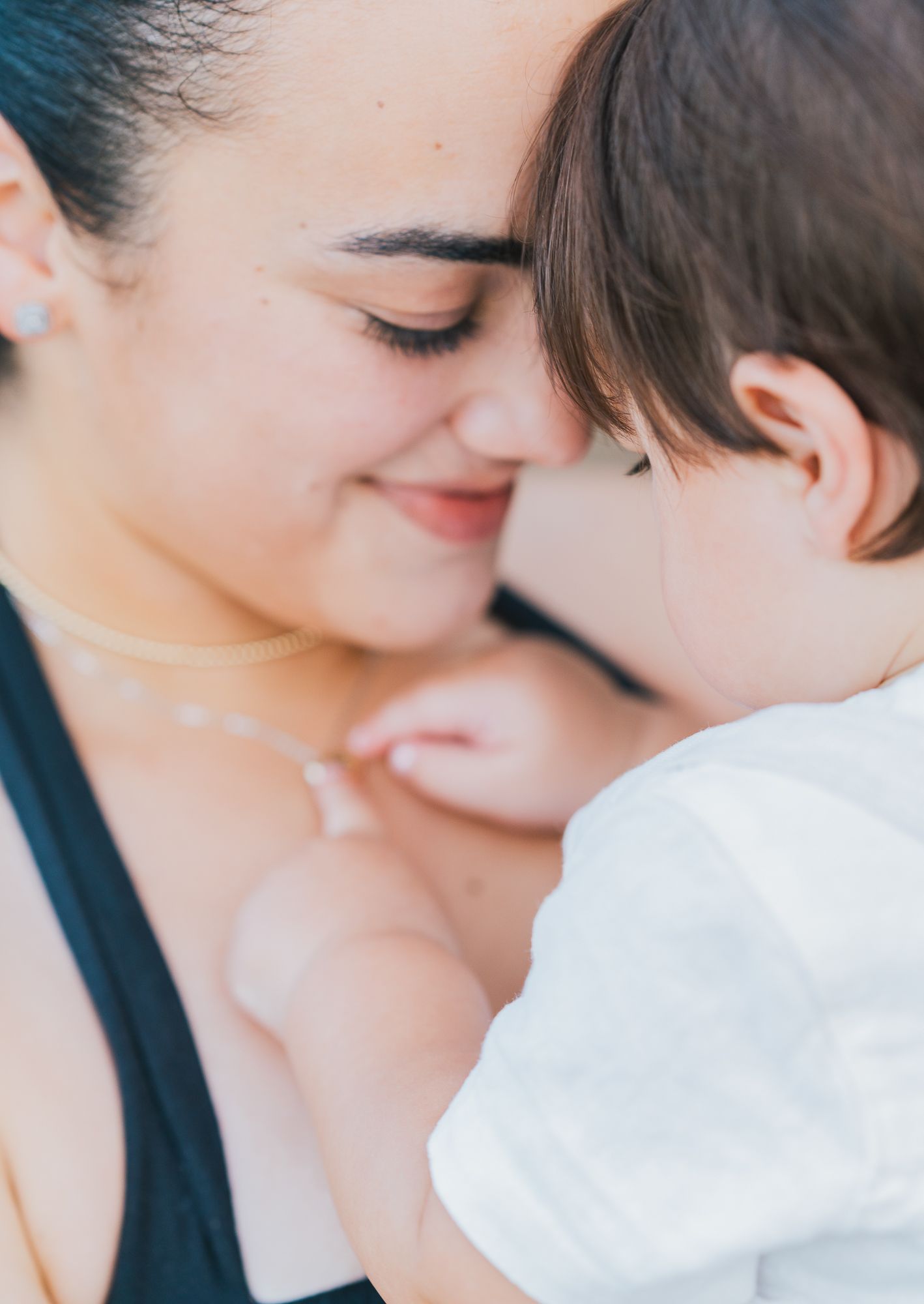 Mother and baby touching foreheads as the baby reaches for her necklace.