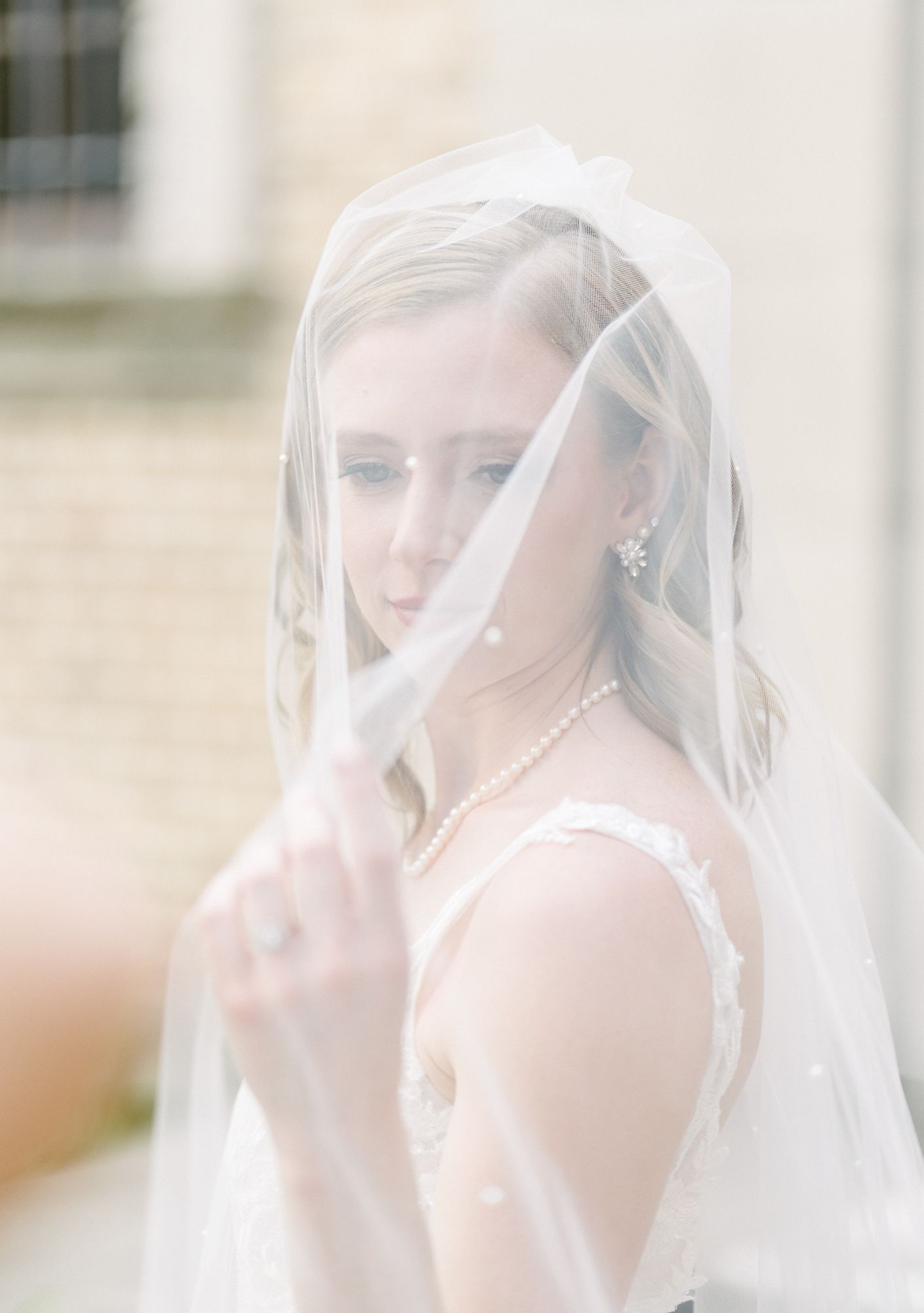 Close-up of a bride looking through a sheer veil, wearing pearl jewelry.