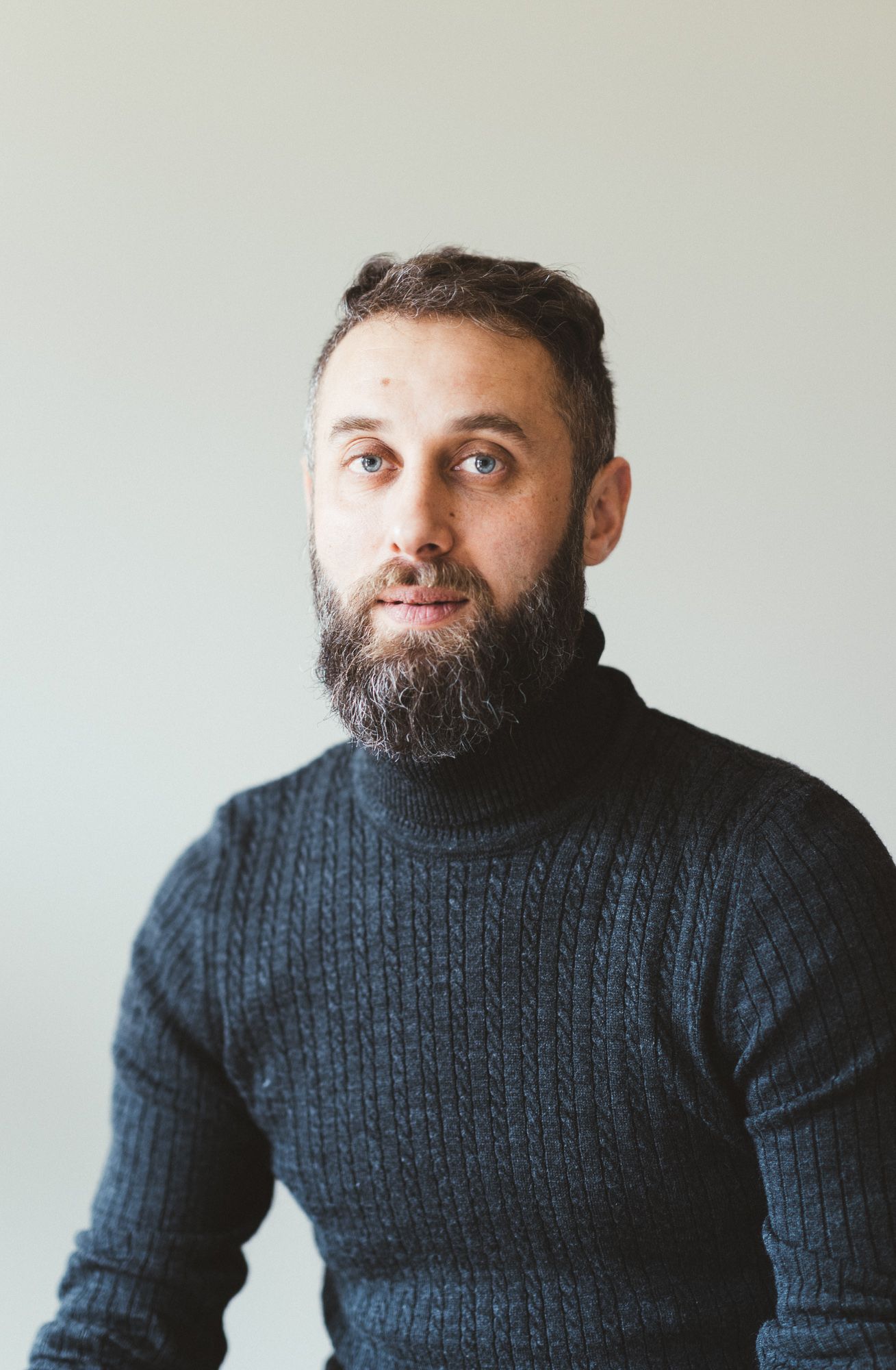 Man in a dark knit turtleneck looking at the camera in soft window light.