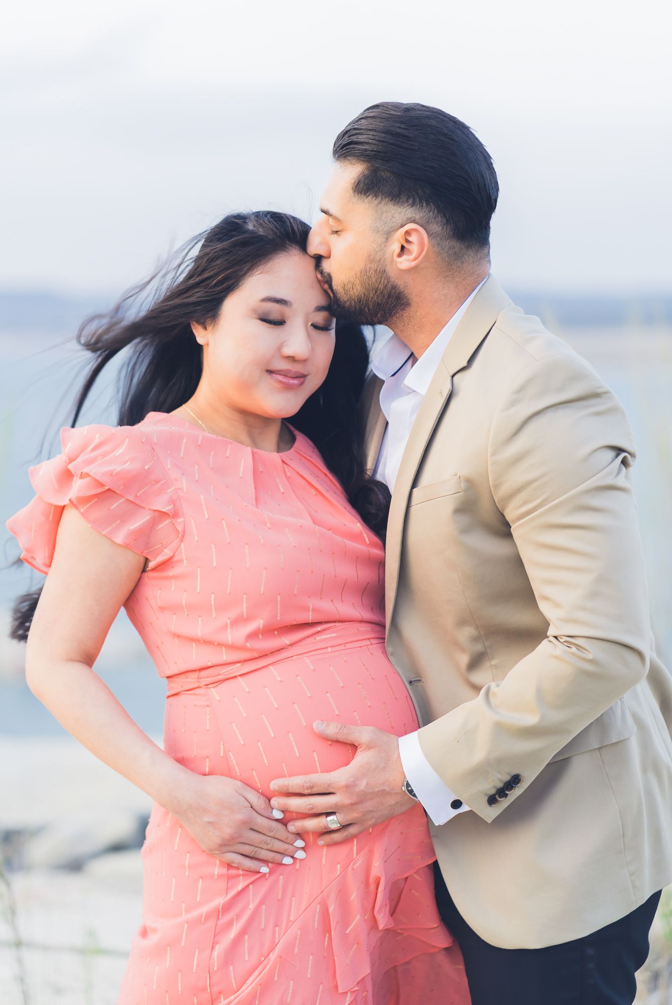 Man kissing his pregnant partner’s forehead as they rest their hands on her belly.