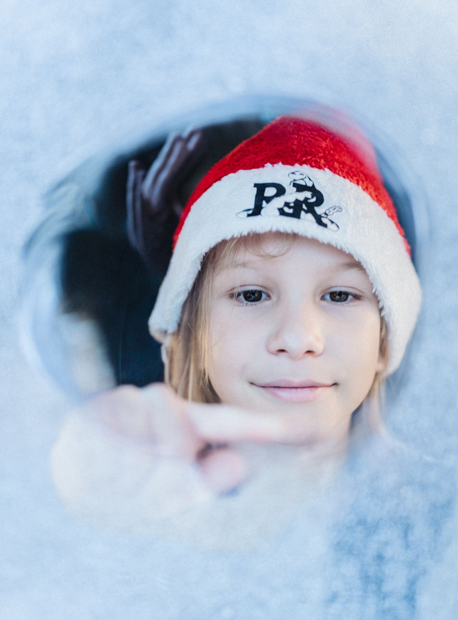 Child in a Santa hat reaching toward the camera through soft white fabric during a Christmas lifestyle session in Austin, Texas.