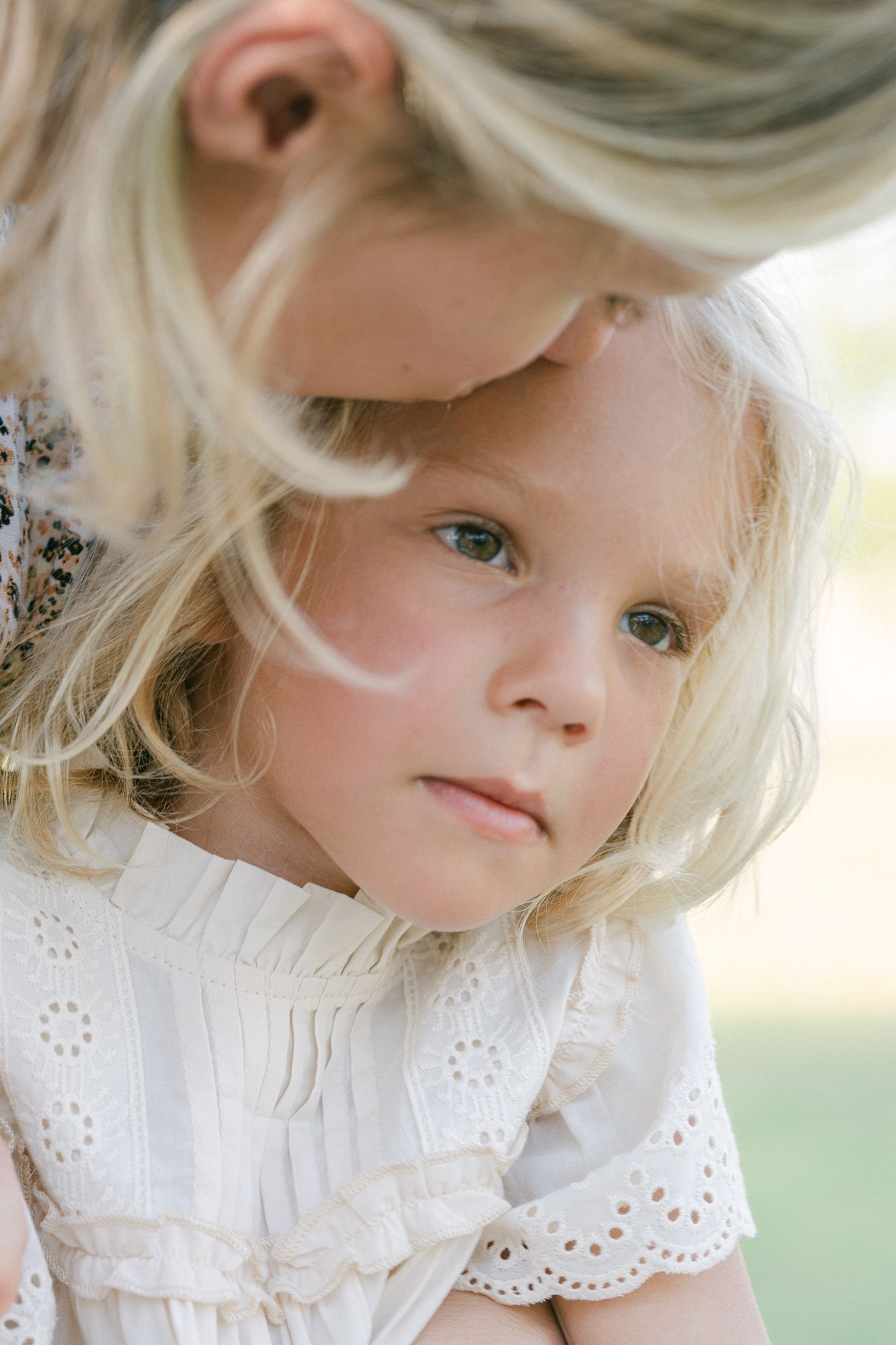 Close-up of a mother kissing her daughter’s forehead as the child gazes into the distance.