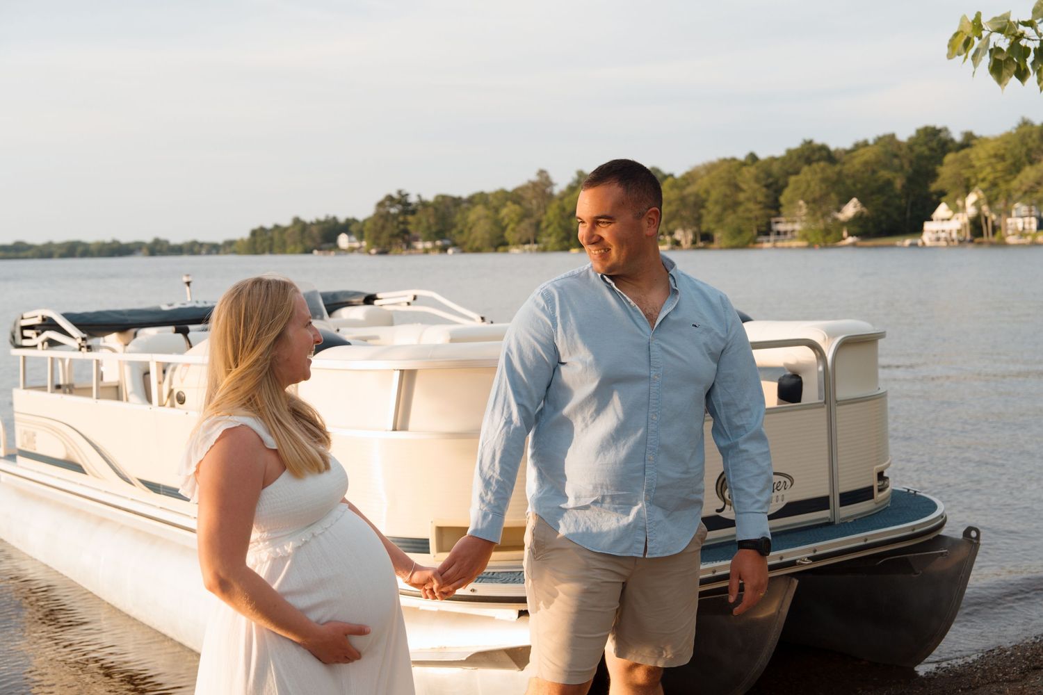 A couple standing on a dock by a boat during a sunny afternoon on the lake.