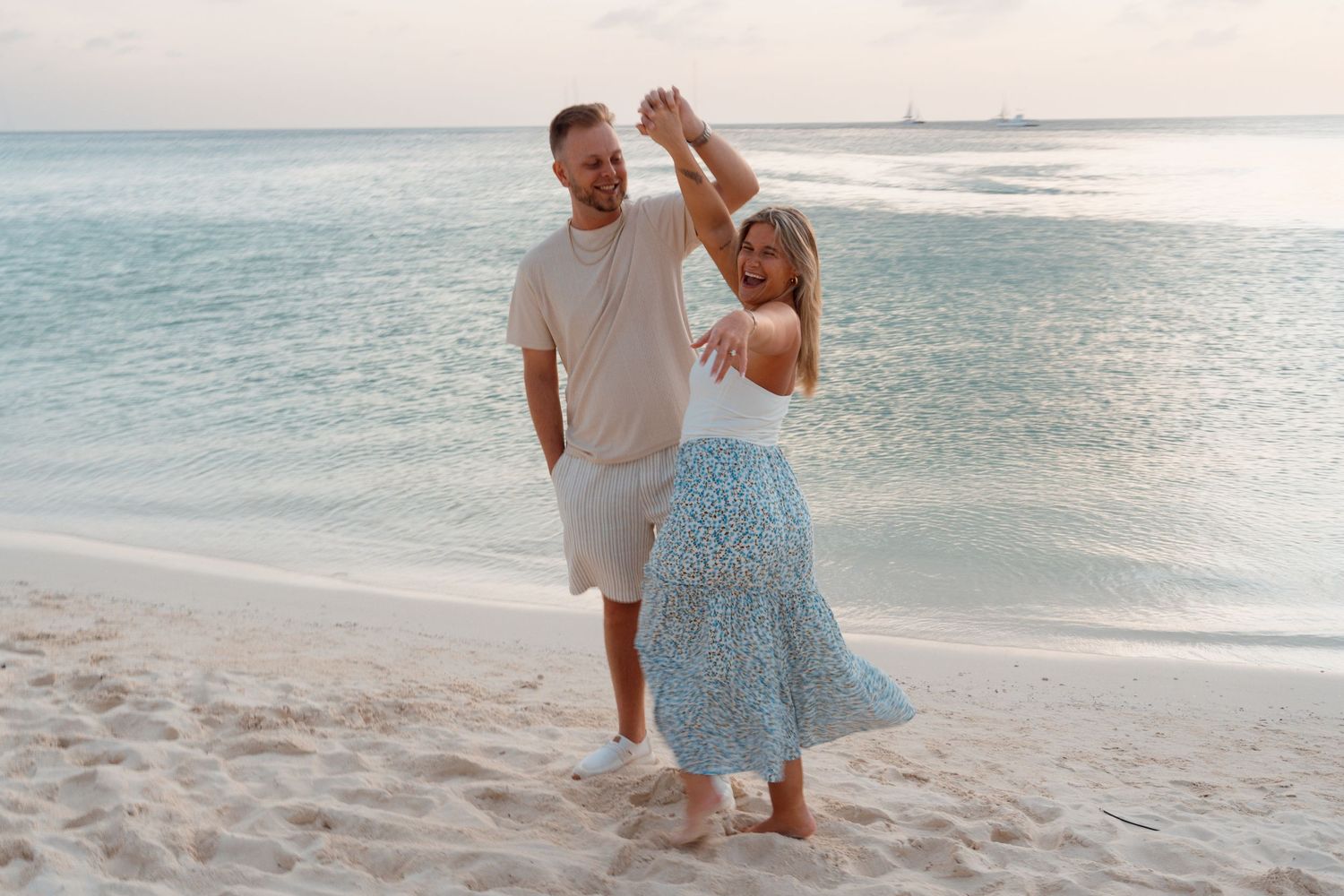 A couple dances together on a pristine beach at sunset with turquoise ocean waters in the background.
